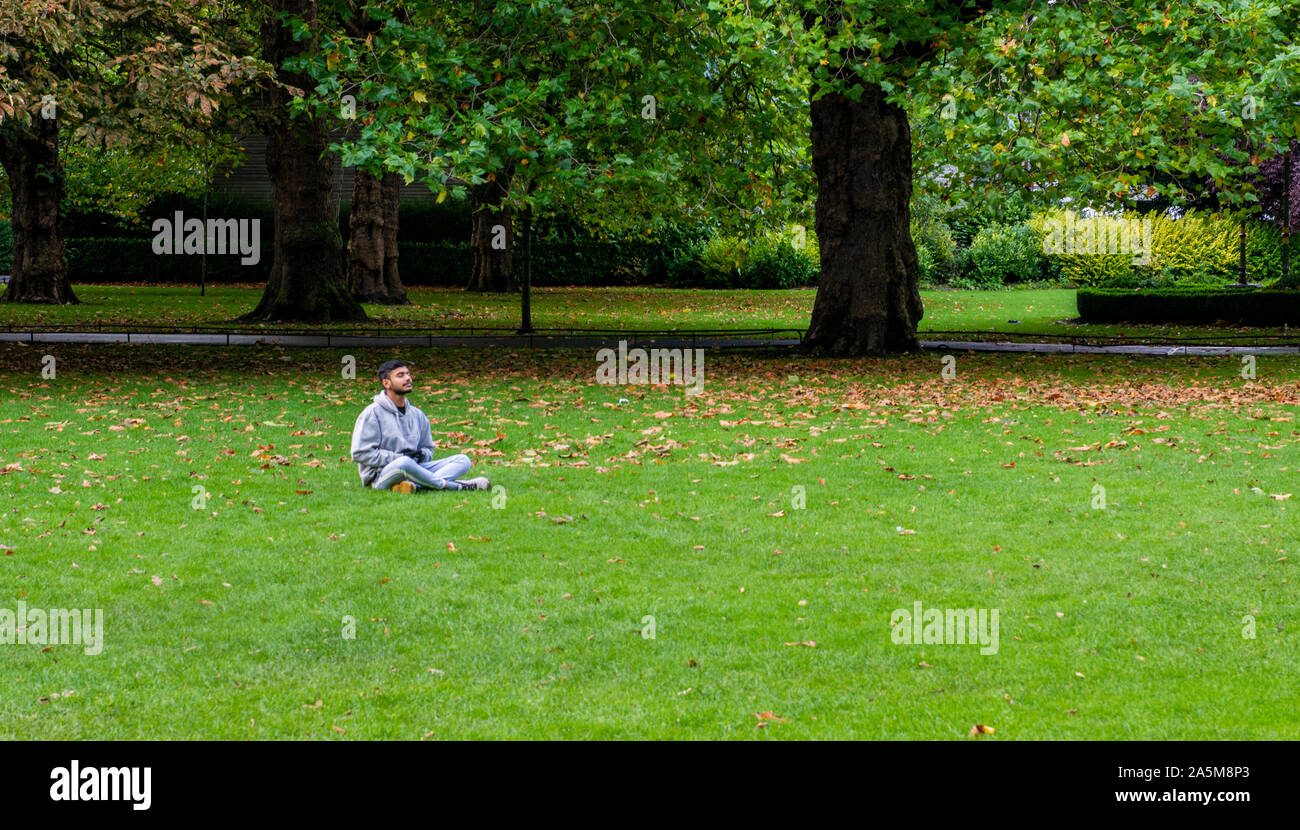 Man meditating on grass in park, Dublin, Irlande, UK Banque D'Images