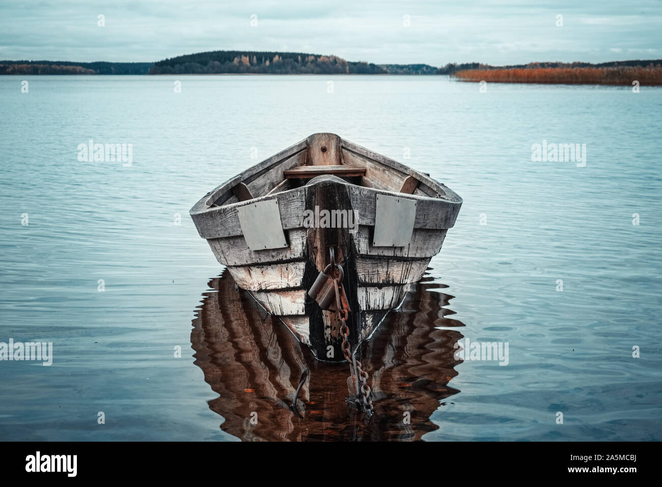 Bateau à rames en bois reflet dans un lac encore eau au crépuscule. Banque D'Images