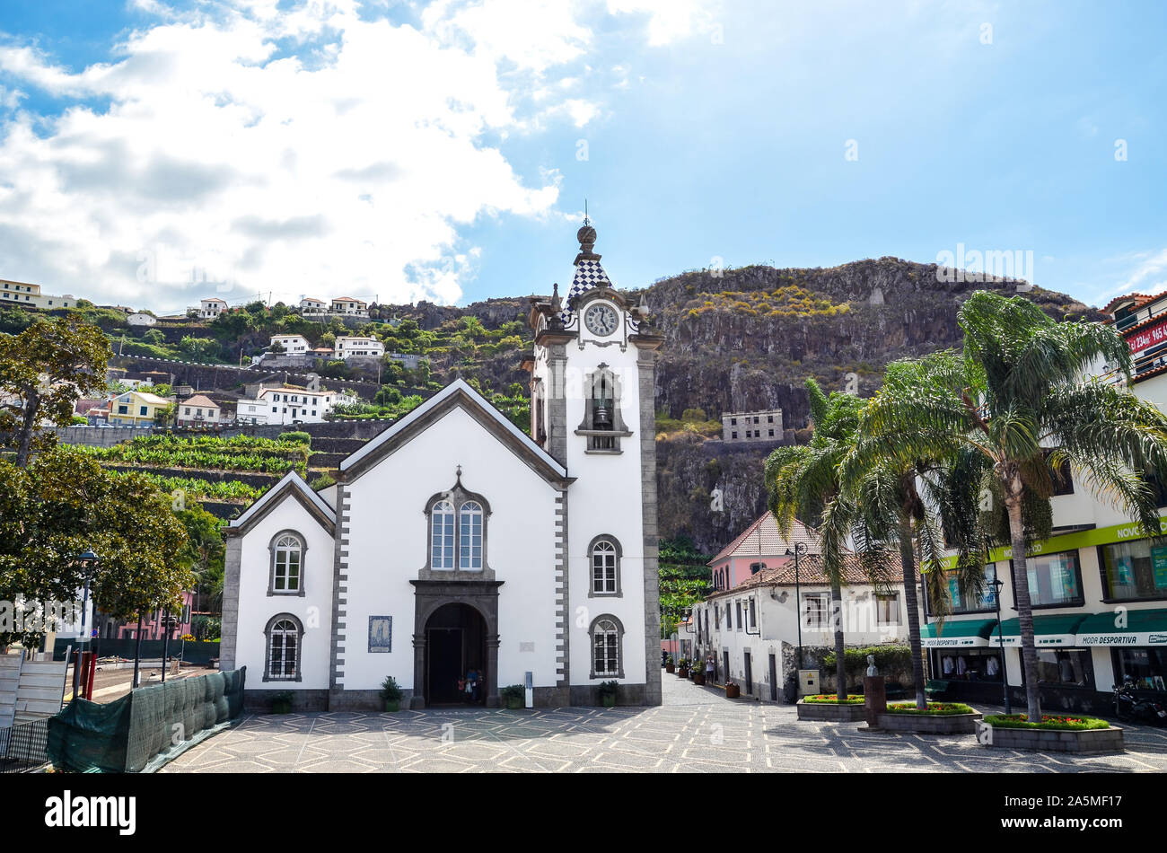 Ribeira Brava, Madeira, Portugal - Sep 9, 2019 : Belle église catholique romaine dans le centre-ville. Palmiers sur la place. Les plantations de banane sur une colline rocheuse à l'arrière-plan. Banque D'Images