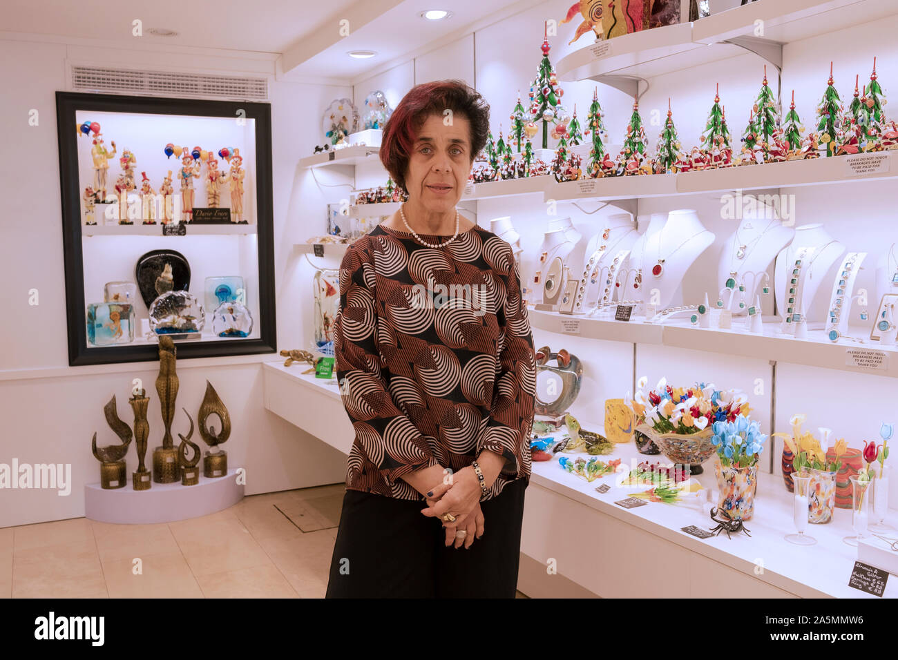 Posée portrait d'une femme de 60 ans qui vend des articles en verre fantaisie Morano dans un magasin situé au large de la Place San Marco à Venise, Italie. Banque D'Images