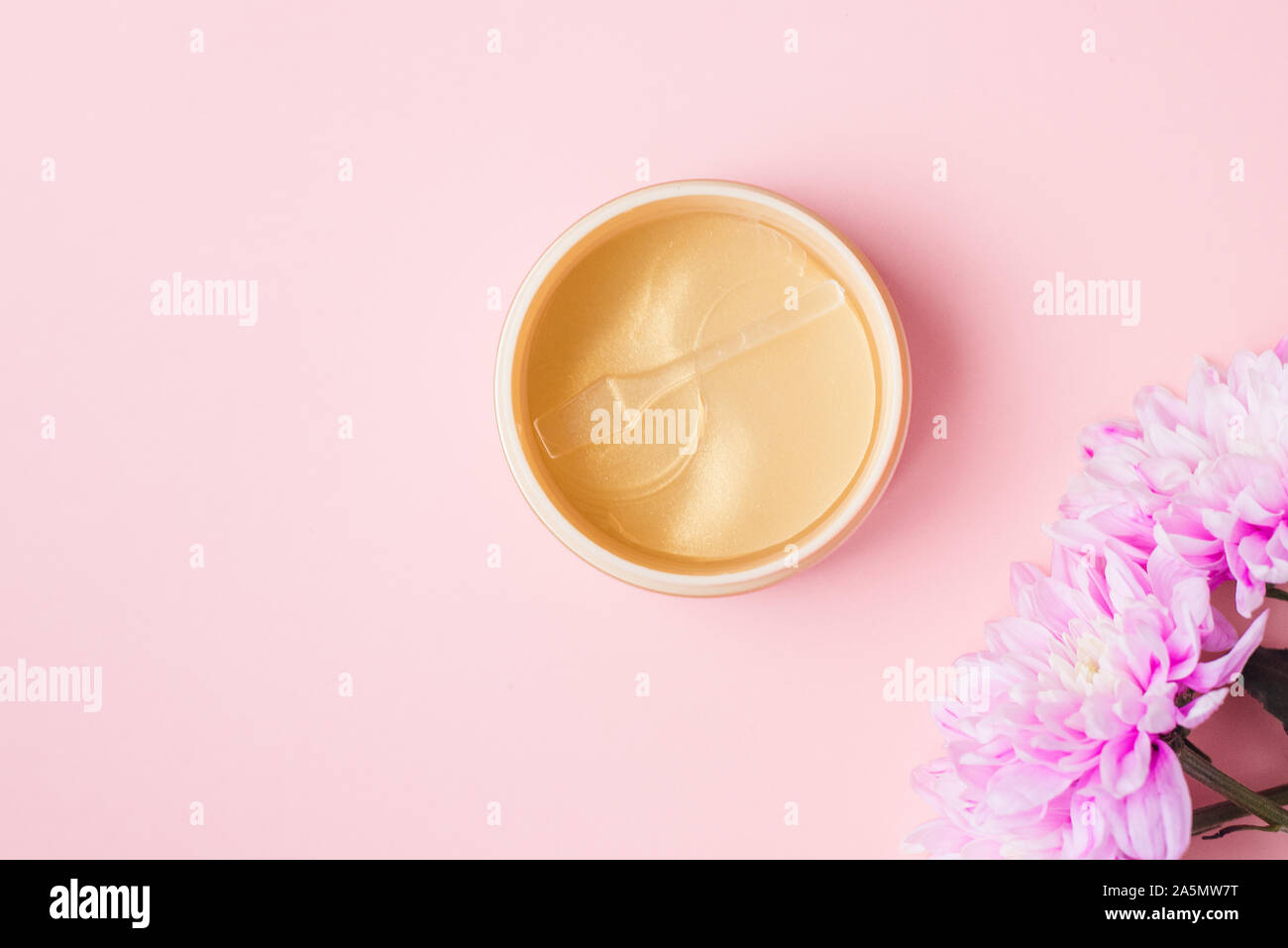 Les correctifs d'or sur un fond pastel rose à côté des fleurs de chrysanthème. Extrait de fleur naturelle cosmétiques, de la beauté et de la mode. Correctifs pour hydrater dans un bocal, mettre à plat, vue du dessus. Banque D'Images