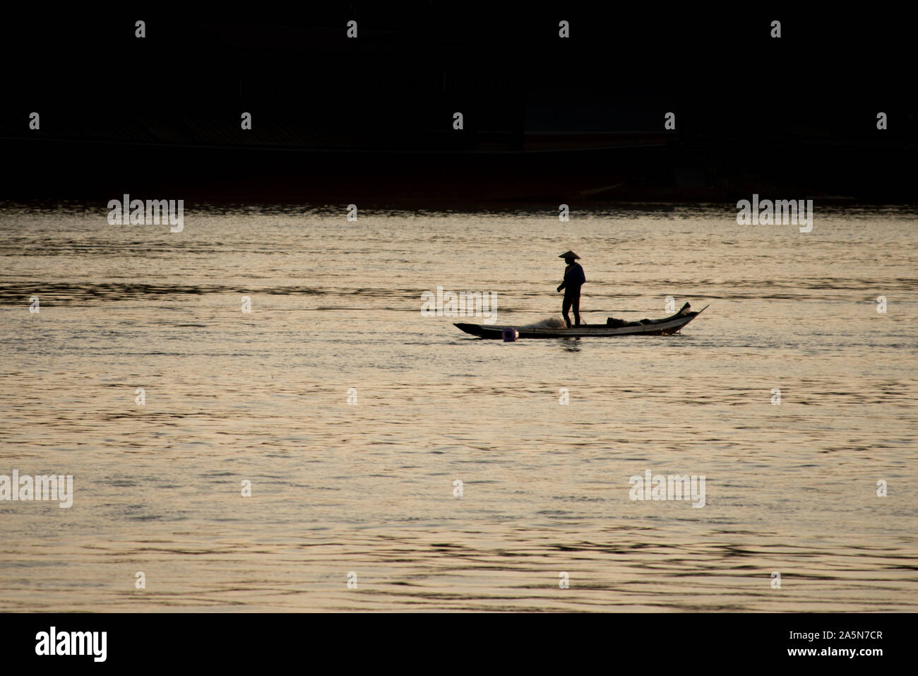 Pêcheur sur un petit bateau de pêche au coucher du soleil sur le Mékong près de Luang Prabang, Laos. Banque D'Images