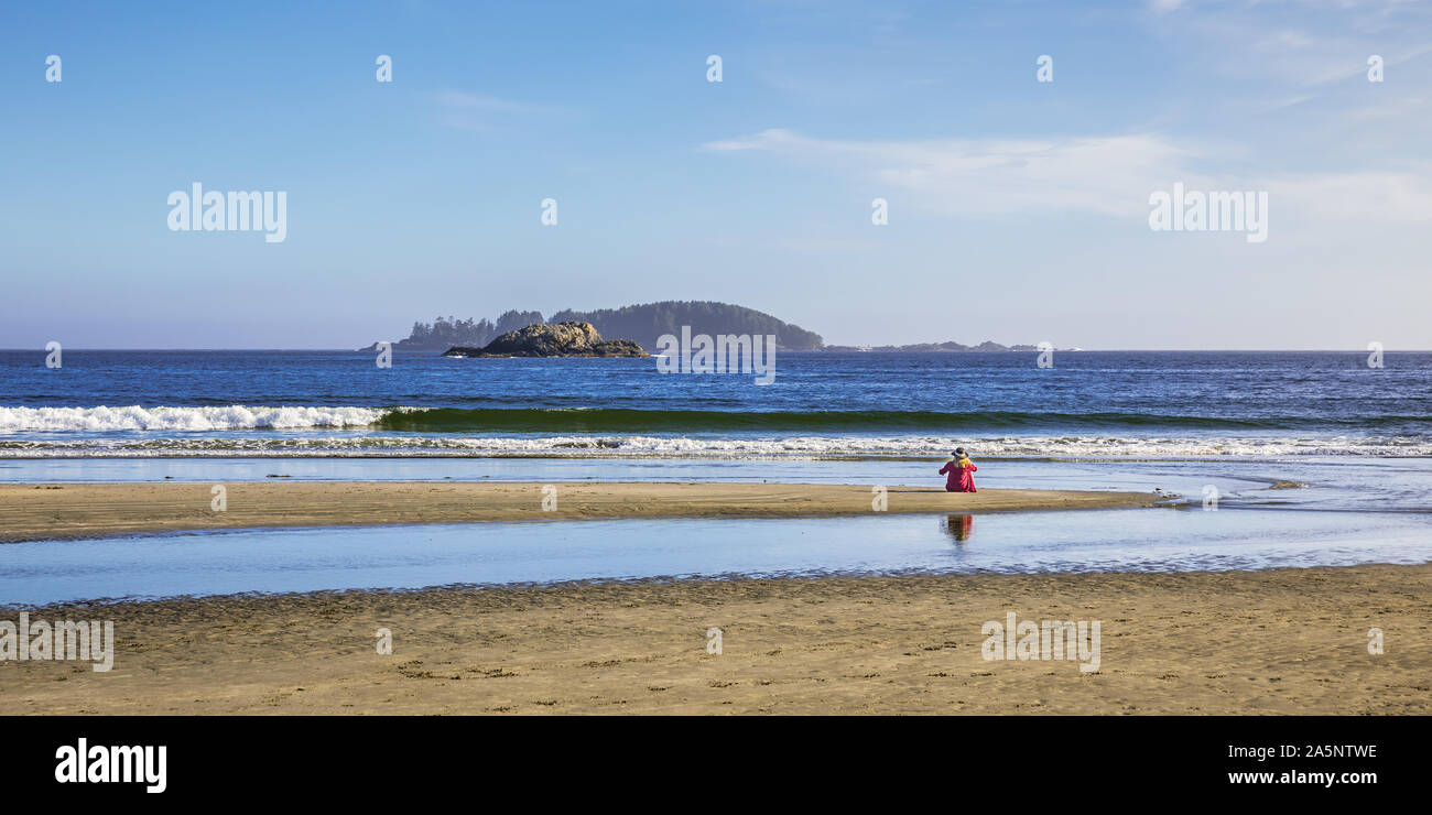 View of woman with Hat et Red shirt assis tout seul sur la plage à regarder l'ouest de l'océan Pacifique près de Tofino sur l'île de Vancouver Banque D'Images