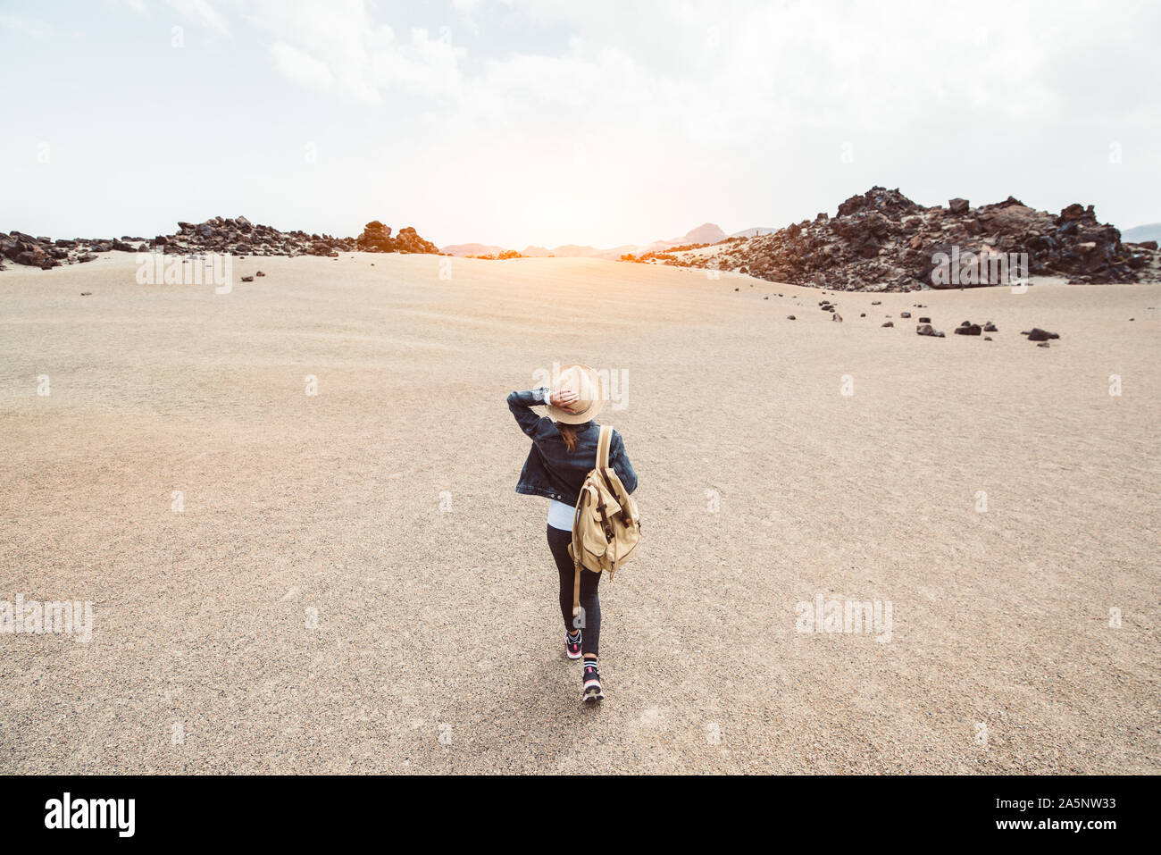 Traveller woman walking dans un désert rocailleux holding hat et son sac à dos au coucher du soleil Banque D'Images