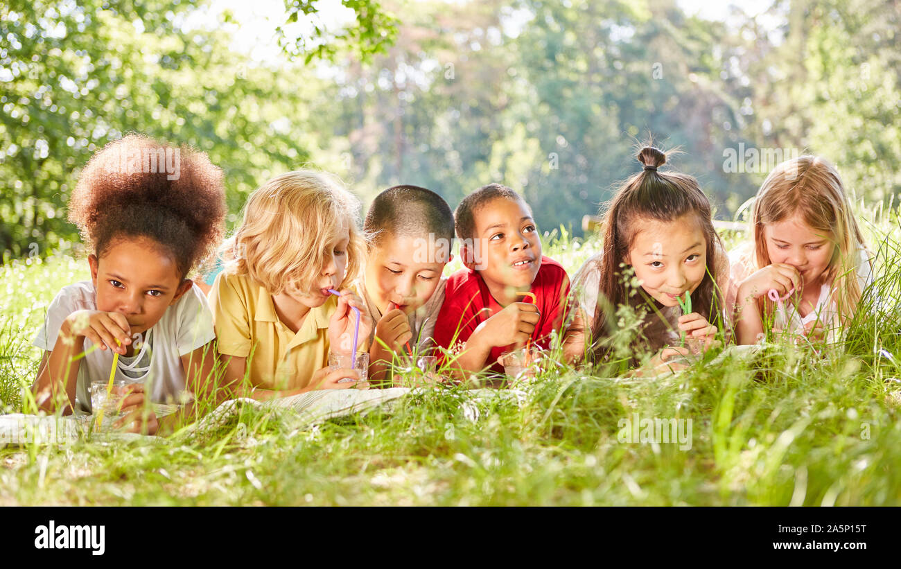 Les enfants multiculturels boire de l'eau avec de la paille sur la prairie d'été Banque D'Images