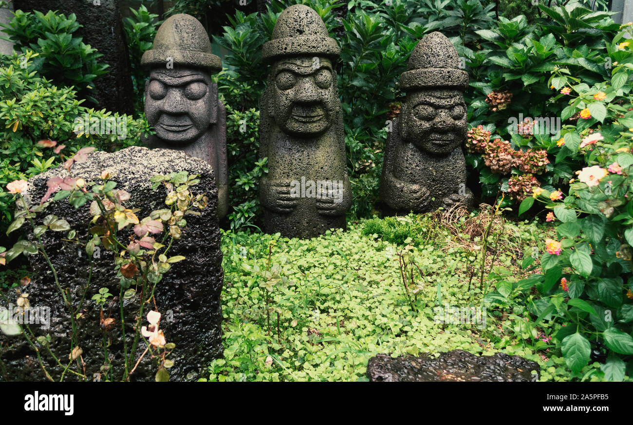 L'île de Jeju, Corée du Sud, le 06 septembre 2019 : Trois sculpturs de Dol Hareubangs dans les buissons et fleurs à jour de pluie Banque D'Images