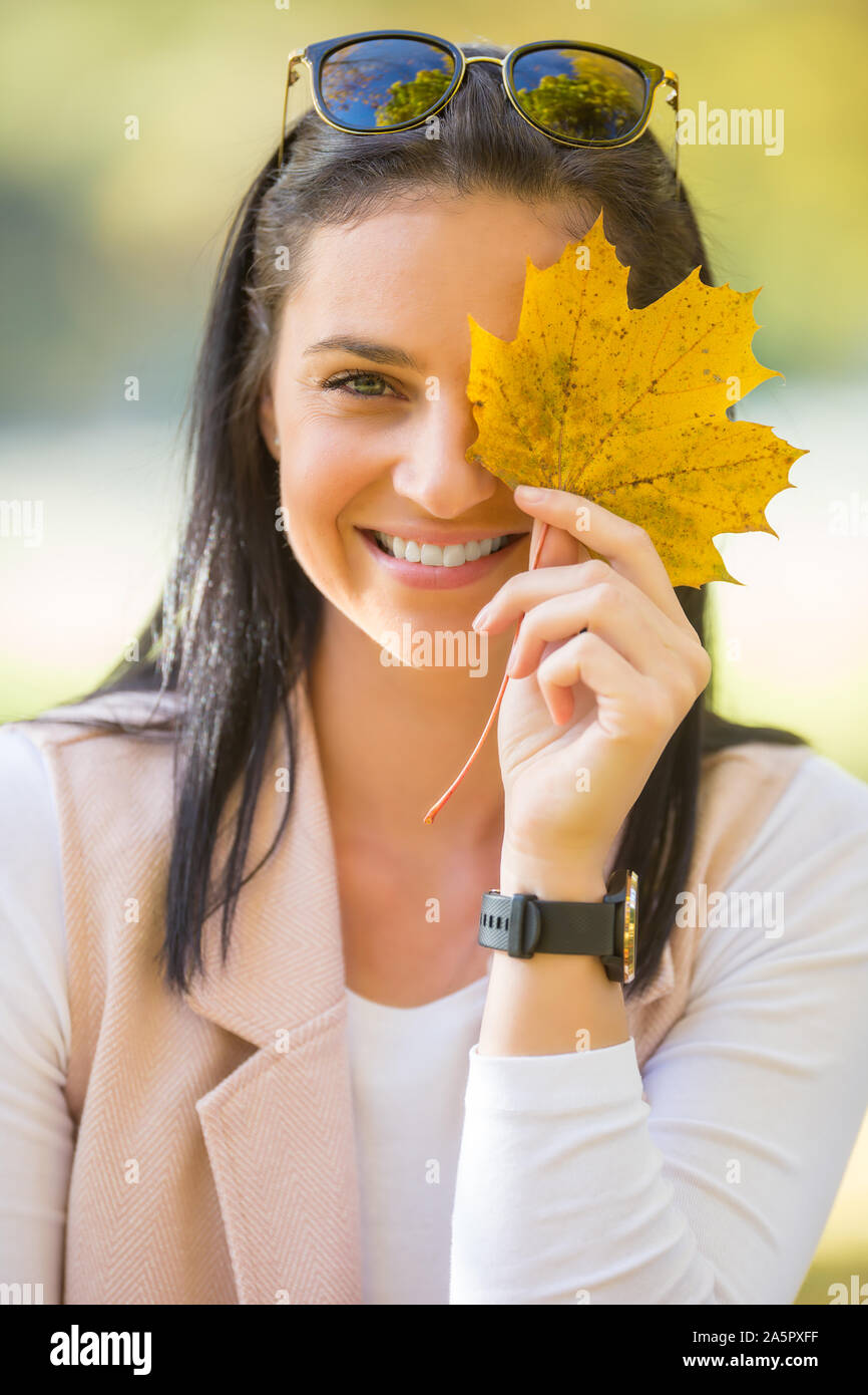 Happy woman with beautiful smile contient des feuilles d'automne jaune en face de visage Banque D'Images