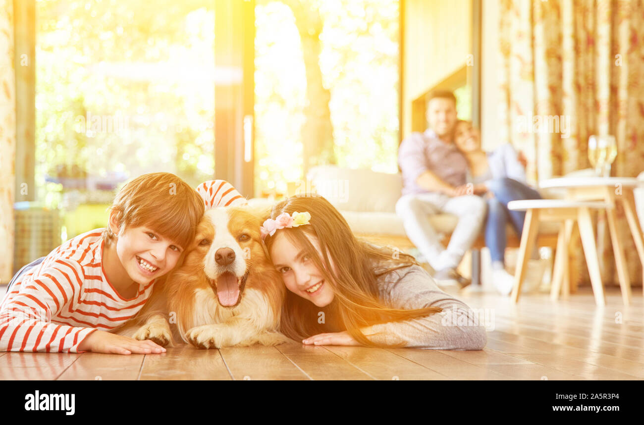 Deux enfants câlin avec chien comme animal de compagnie dans le salon avec les parents dans l'arrière-plan Banque D'Images