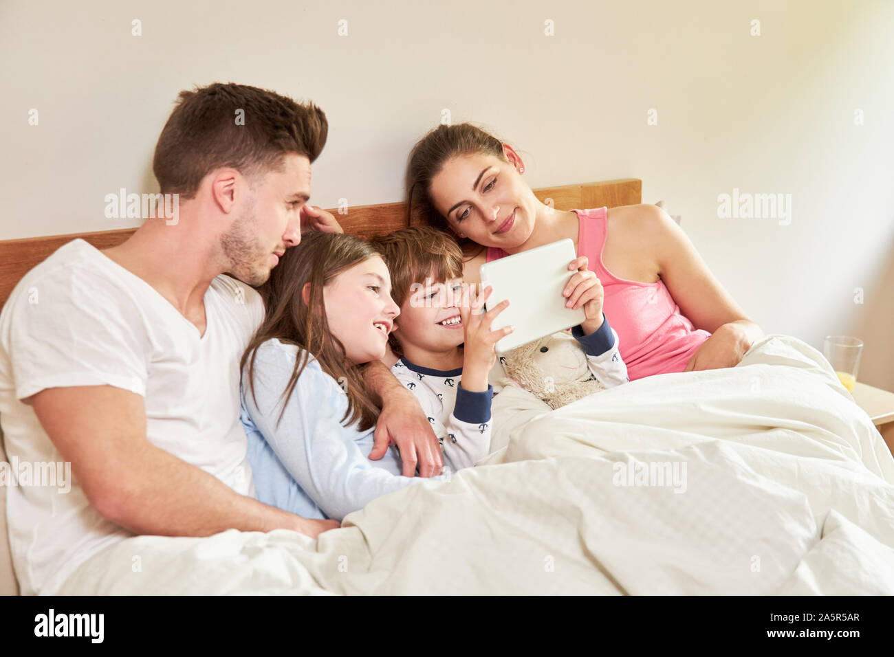 Les enfants et les parents à l'aide de l'ordinateur tablette dans le lit regardant la vidéo ou surfer sur le web Banque D'Images