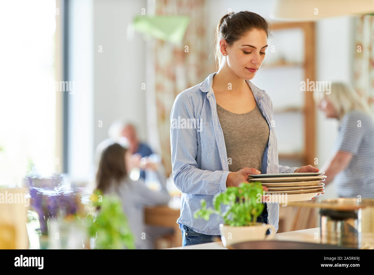 Jeune femme comme une femme au foyer le nettoyage de la vaisselle avec la famille dans l'arrière-plan Banque D'Images