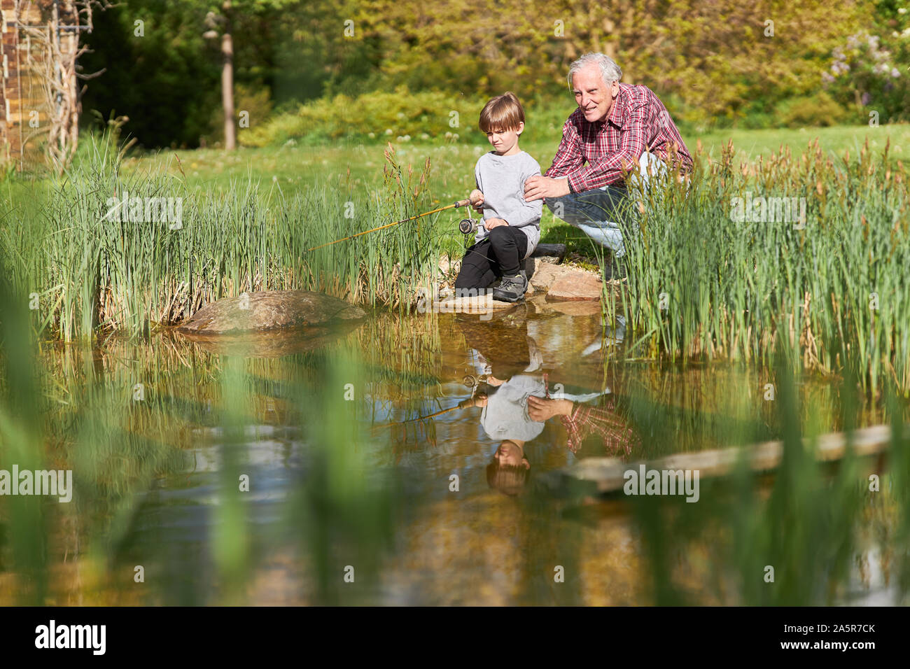 Grand-père et petit-fils de canne à pêche pêche ensemble par le lac en été Banque D'Images