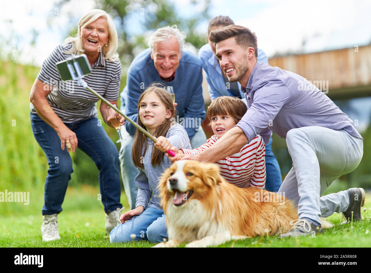 Famille élargie avec les grands-parents et deux enfants, avec chien selfies dans le jardin Banque D'Images