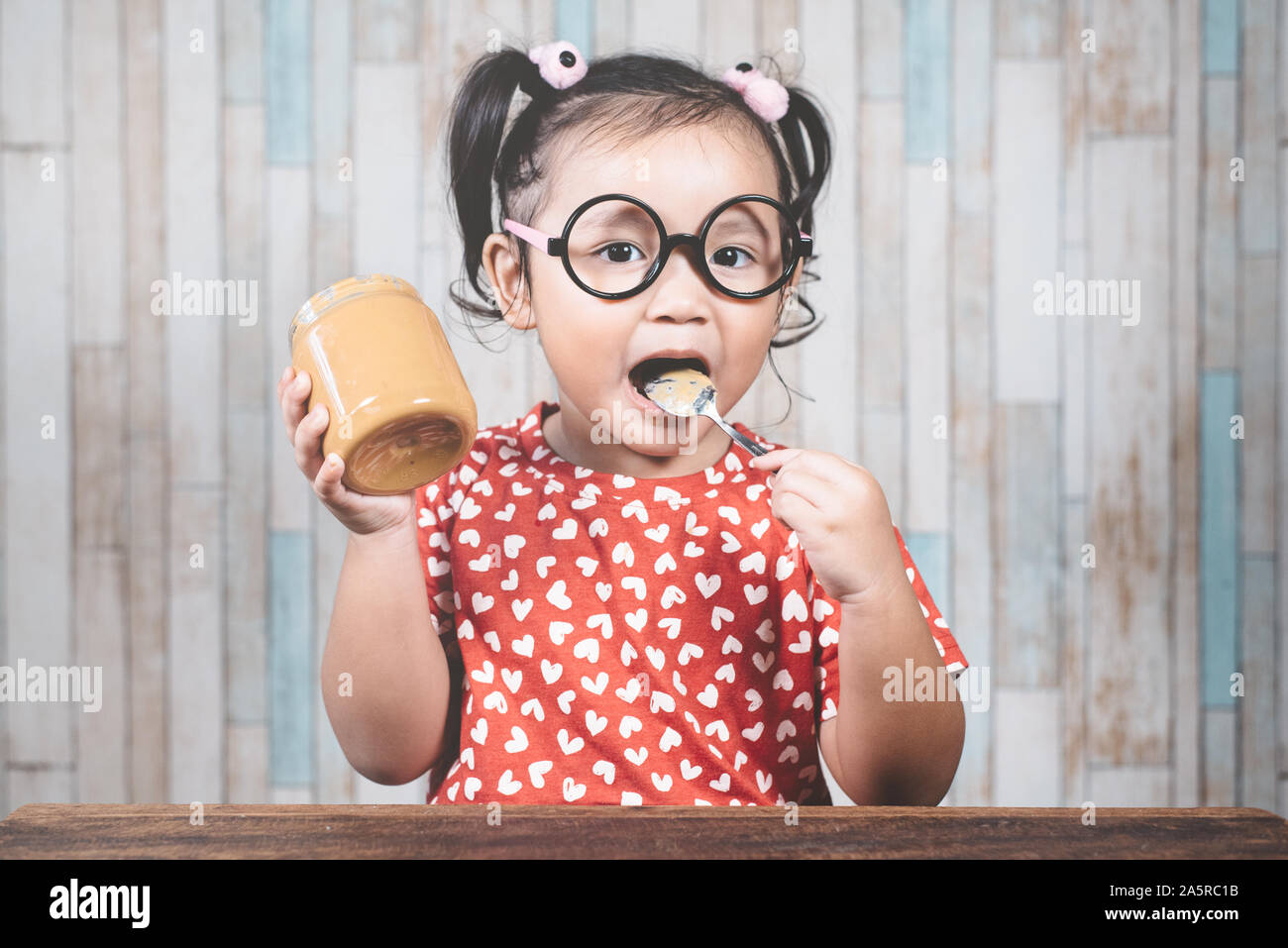 Little asian girl holding et profiter de beurre d'arachide en pot et une cuillère, Concept de peanut butter lover Banque D'Images