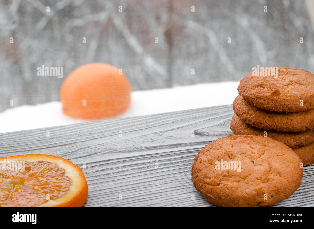 Biscuits orange ronde avec des fruits confits et une tranche d'orange juteuse allongé sur une table en bois dans le contexte de la forêt d'hiver Banque D'Images