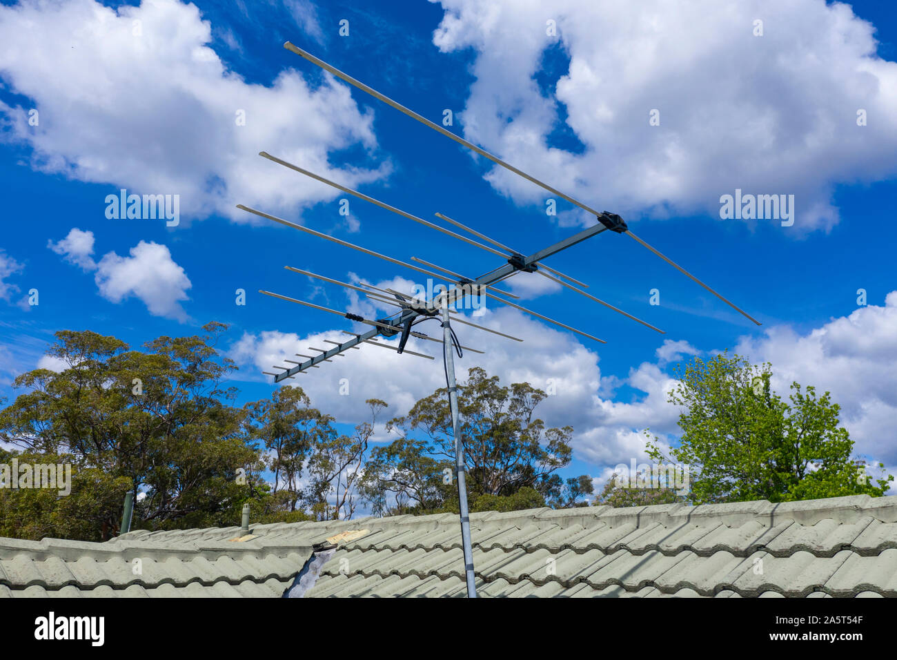 L'antenne de télévision sur un toit vert avec des arbres et un ciel bleu avec des nuages en arrière-plan. Banque D'Images