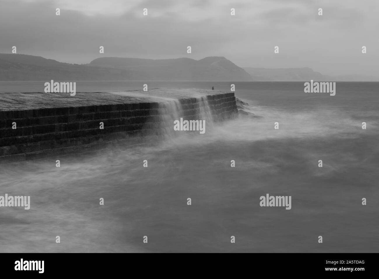 La longue exposition des vagues s'écraser contre le quai à Lyme Regis dans le Dorset en noir et blanc Banque D'Images