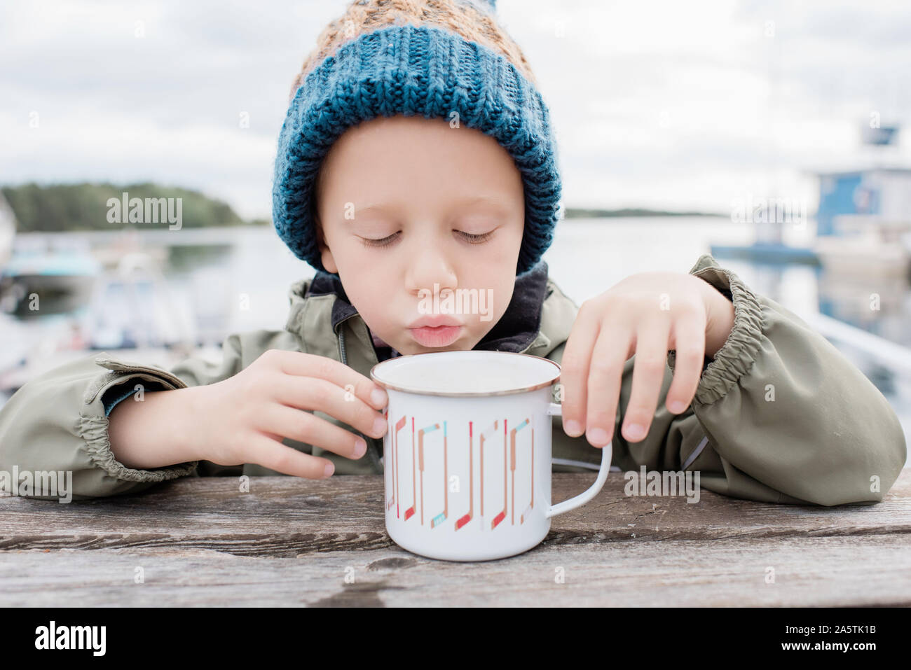 Jeune garçon de boire du chocolat chaud à l'extérieur, sur un banc de pique-nique en hiver Banque D'Images
