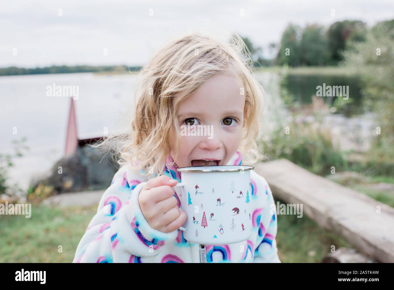 Jeune fille riant de boire un chocolat chaud tout en camping en plein air Banque D'Images