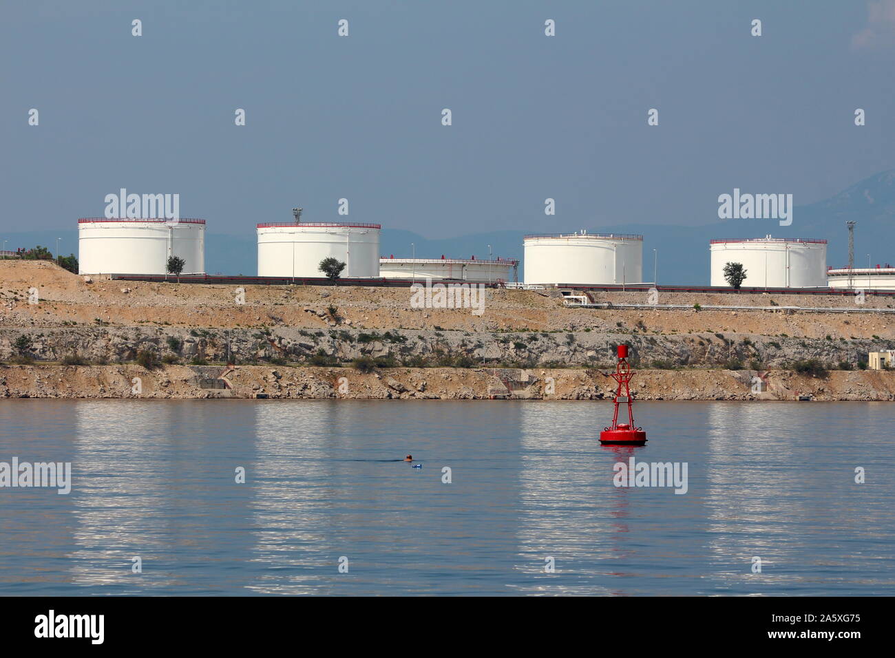 L'homme en face d'une rangée de nouveaux grands réservoirs de la raffinerie de pétrole de métal blanc sur le dessus de la côte rocheuse connecté avec plusieurs tubes en métal Banque D'Images