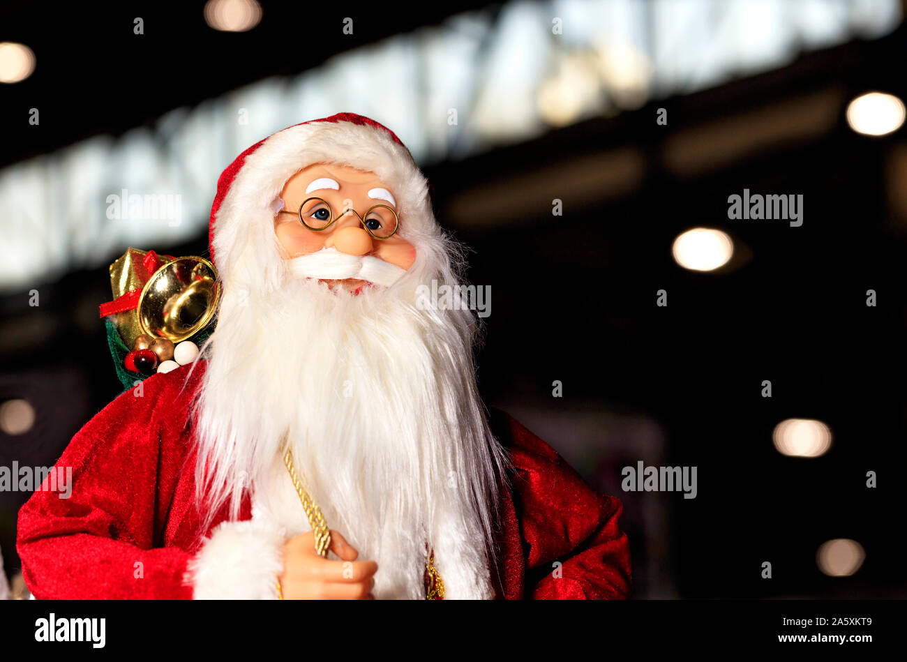 Jouet décoration Père Noël dans un manteau rouge avec un sac de cadeaux sur le dos, souriant, marchant à travers la ville de nuit. Banque D'Images