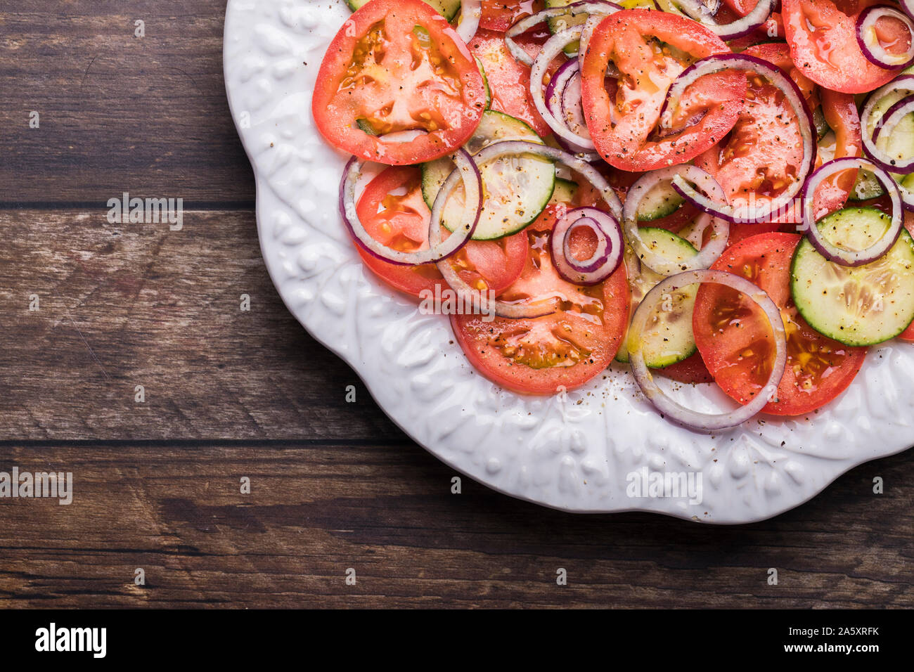 Un frais sain salade avec tomates, concombre, organiques et l'oignon rouge. La salade n'est vu de dessus. C'est sur une table en bois brun rustique, placée dans e Banque D'Images