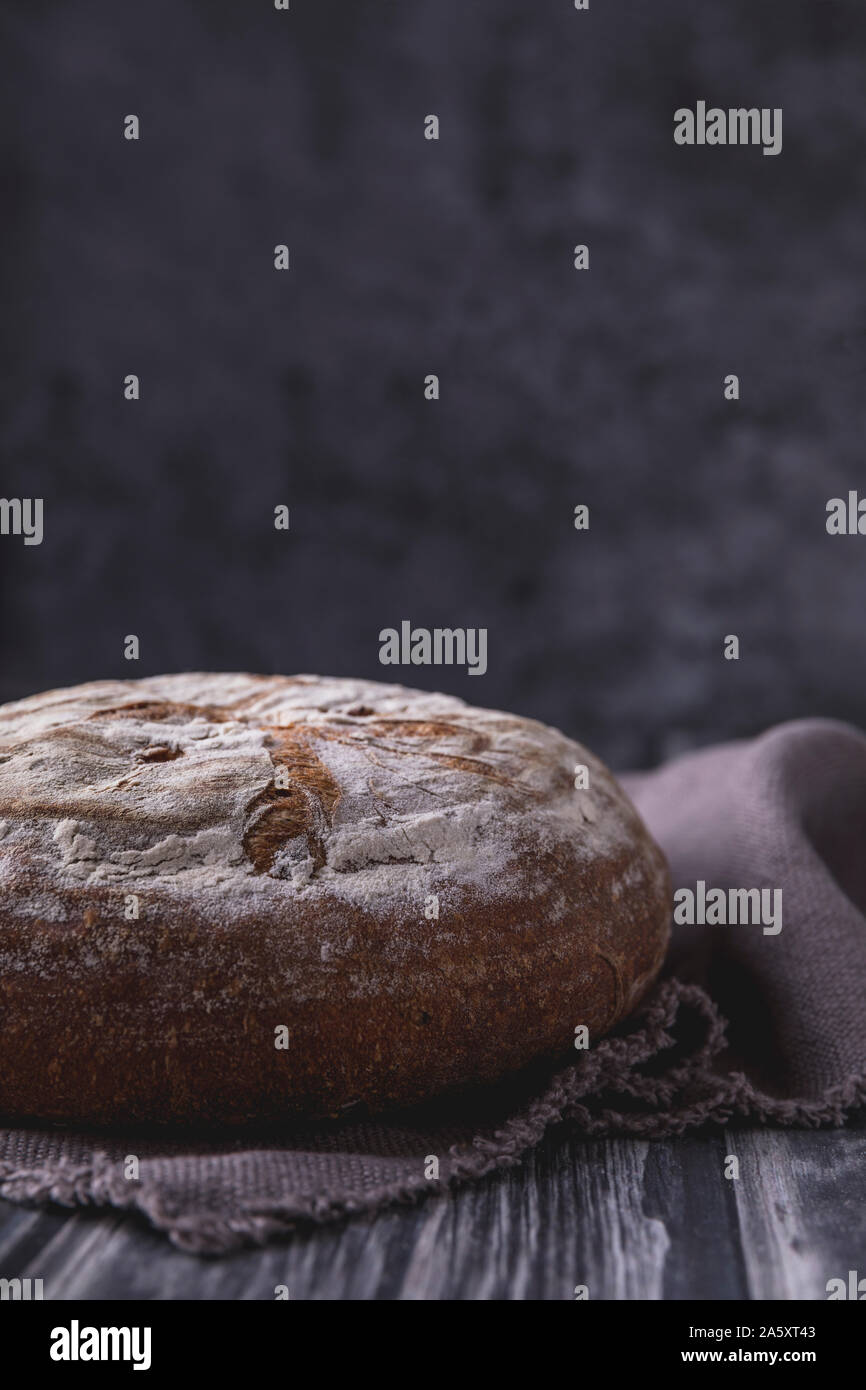 Pain au levain bio faits maison, vue de côté. Le pain rustique fissuré est  mis sur un tissu en lin, qui est sur une table en bois rustique avec gray  backg Photo