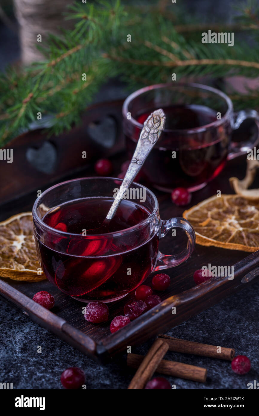 Vin chaud avec des bâtons de cannelle, les oranges et les canneberges séchées. Les verres sont sur un plateau en bois foncé avec une branche d'arbre de pin vert dans l'arrière-plan Banque D'Images