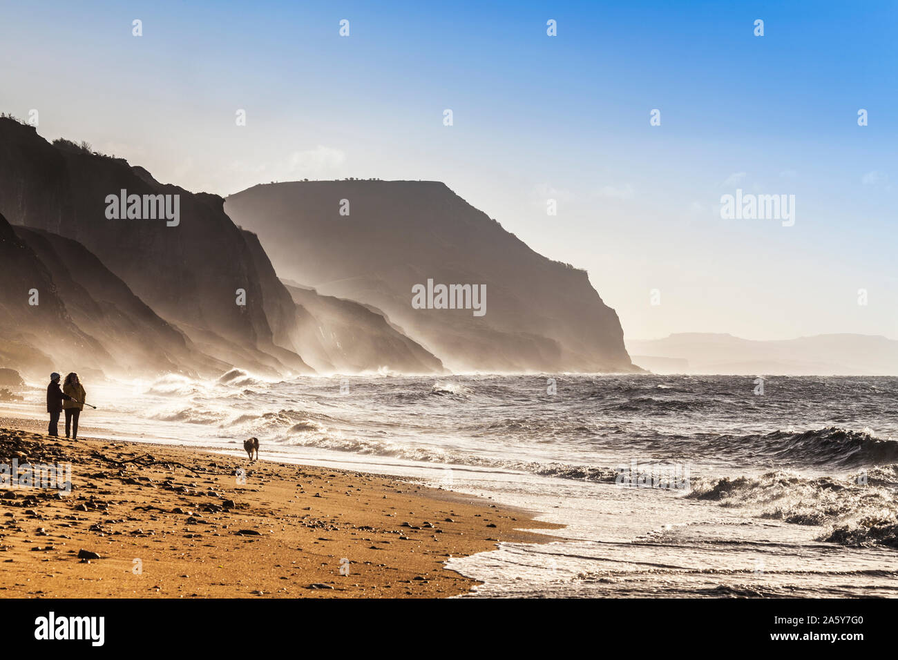 Deux femmes marcher leur chien en Charmouth plage au lever du soleil. Banque D'Images