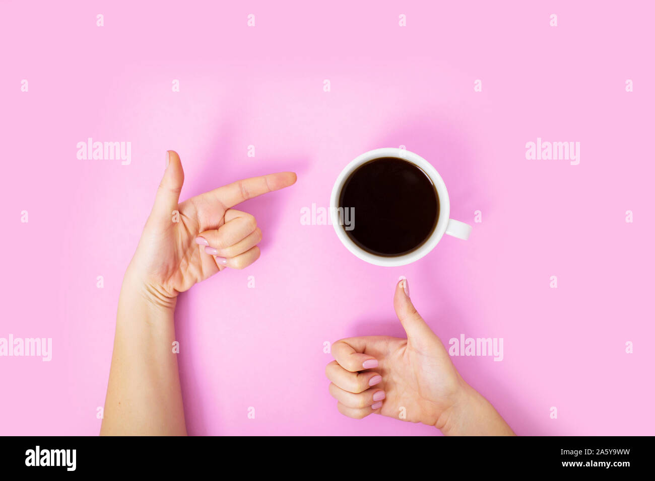 Flatlay avec du café noir dans une tasse blanche sur fond rose. Woman showing thumb up sign, et en pointant du doigt une autre tasse avec la main. Banque D'Images