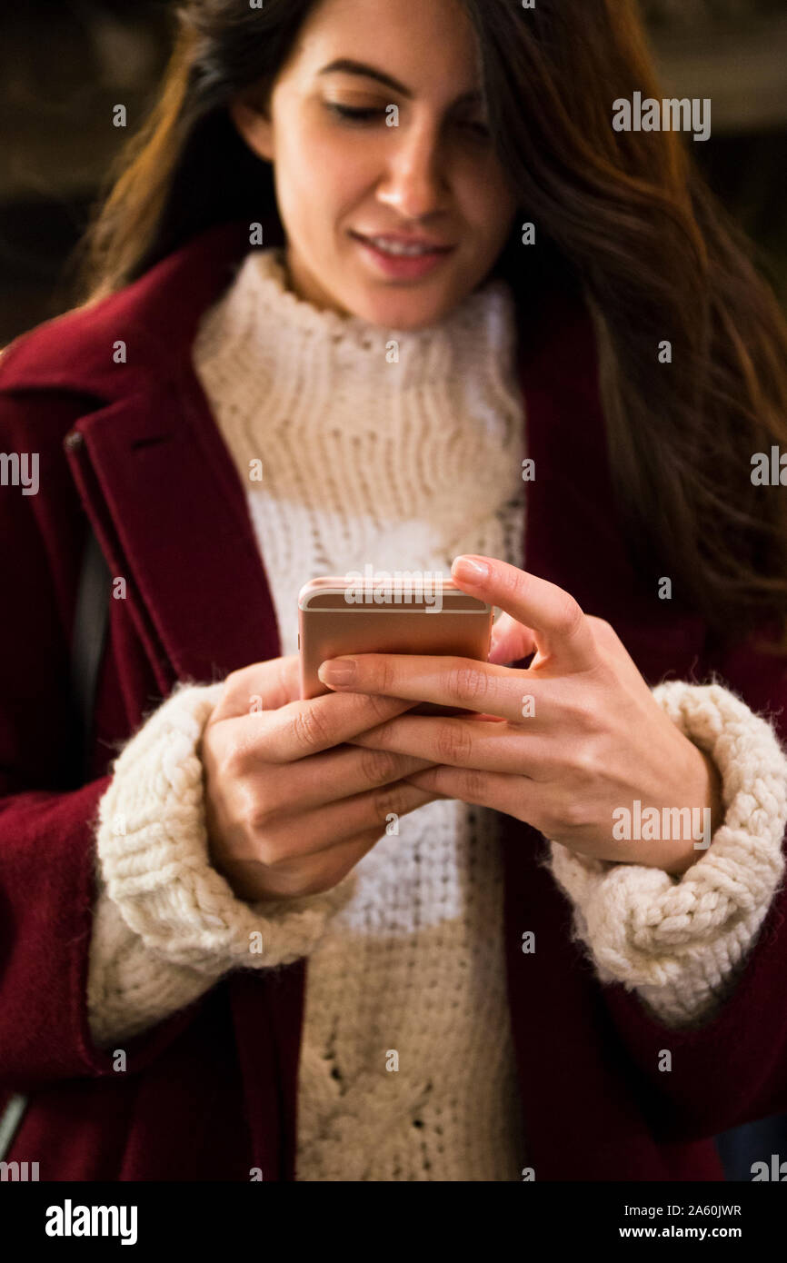 Jeune femme en robe rouge et pull tricoté en utilisant smartphone, close-up Banque D'Images