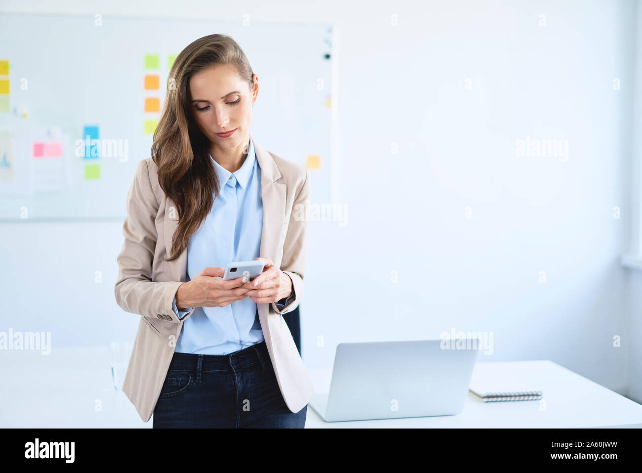 Businesswoman using smartphone leaning on office desk Banque D'Images