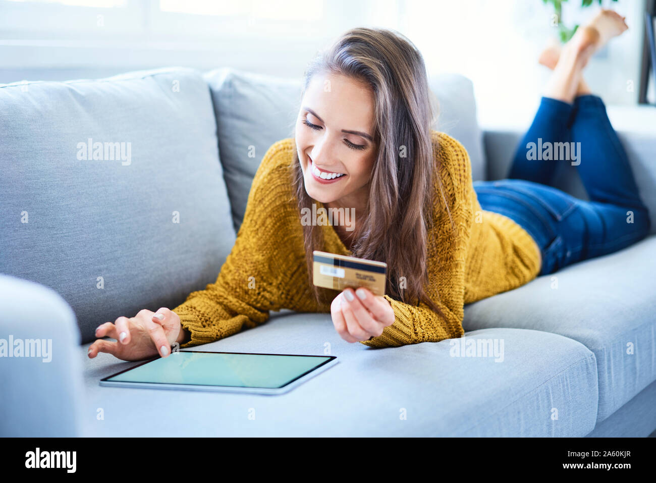 Jeune femme à l'aide de carte de crédit et d'un comprimé à l'acheter en ligne tout en étant allongé sur le canapé Banque D'Images