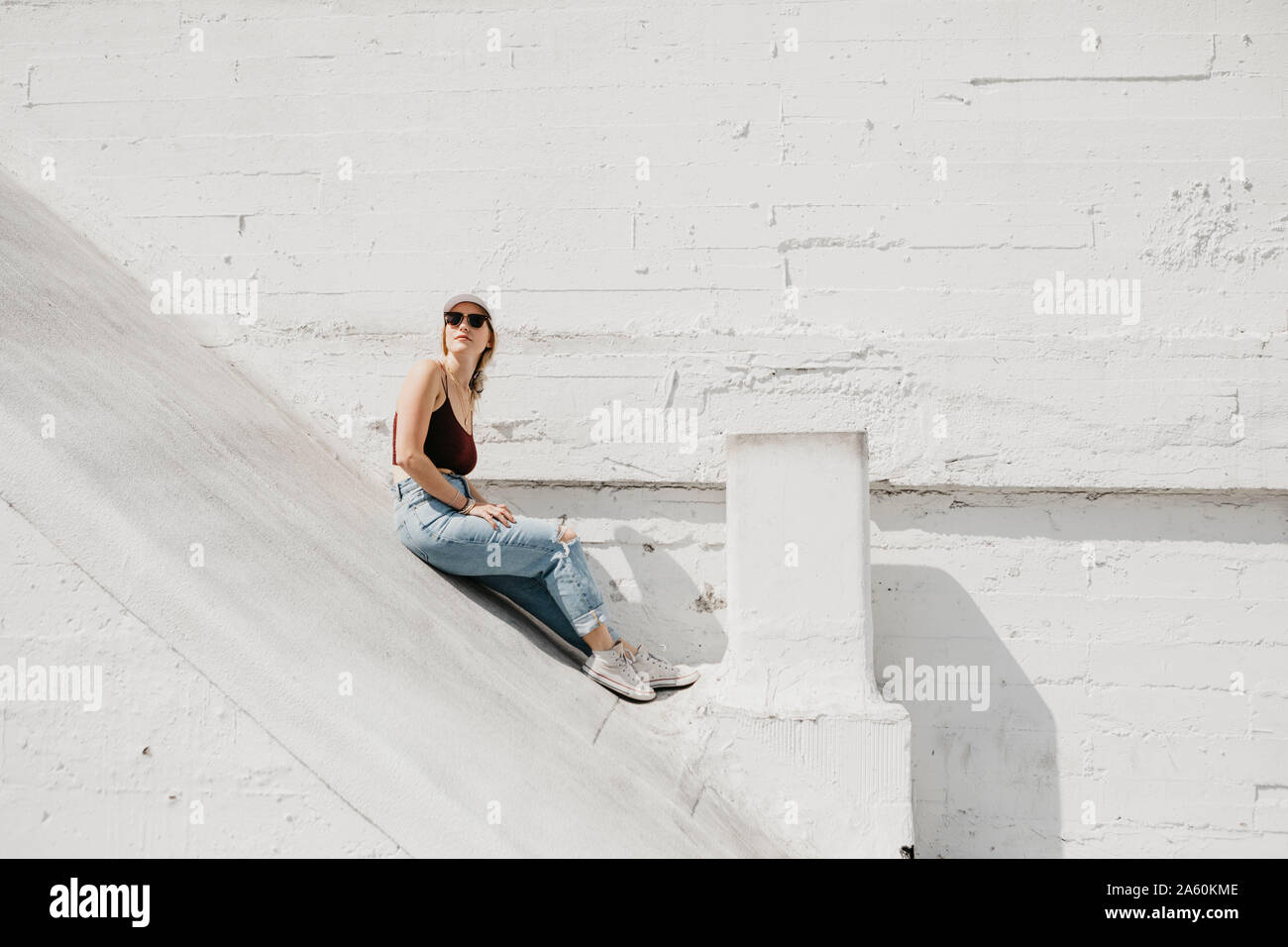Jeune femme assise en face d'un mur blanc à l'extérieur Banque D'Images