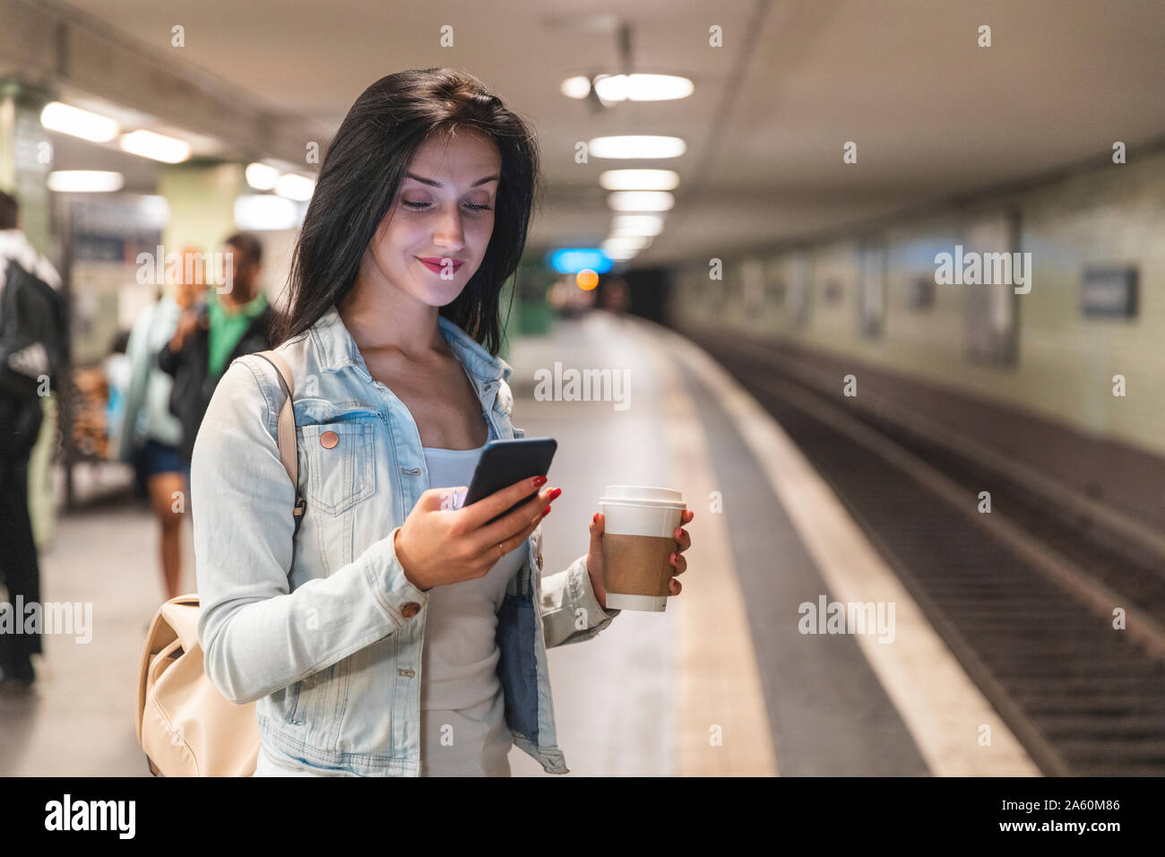 Jeune femme avec téléphone cellulaire à la station de métro en attendant le train, Berlin, Allemagne Banque D'Images