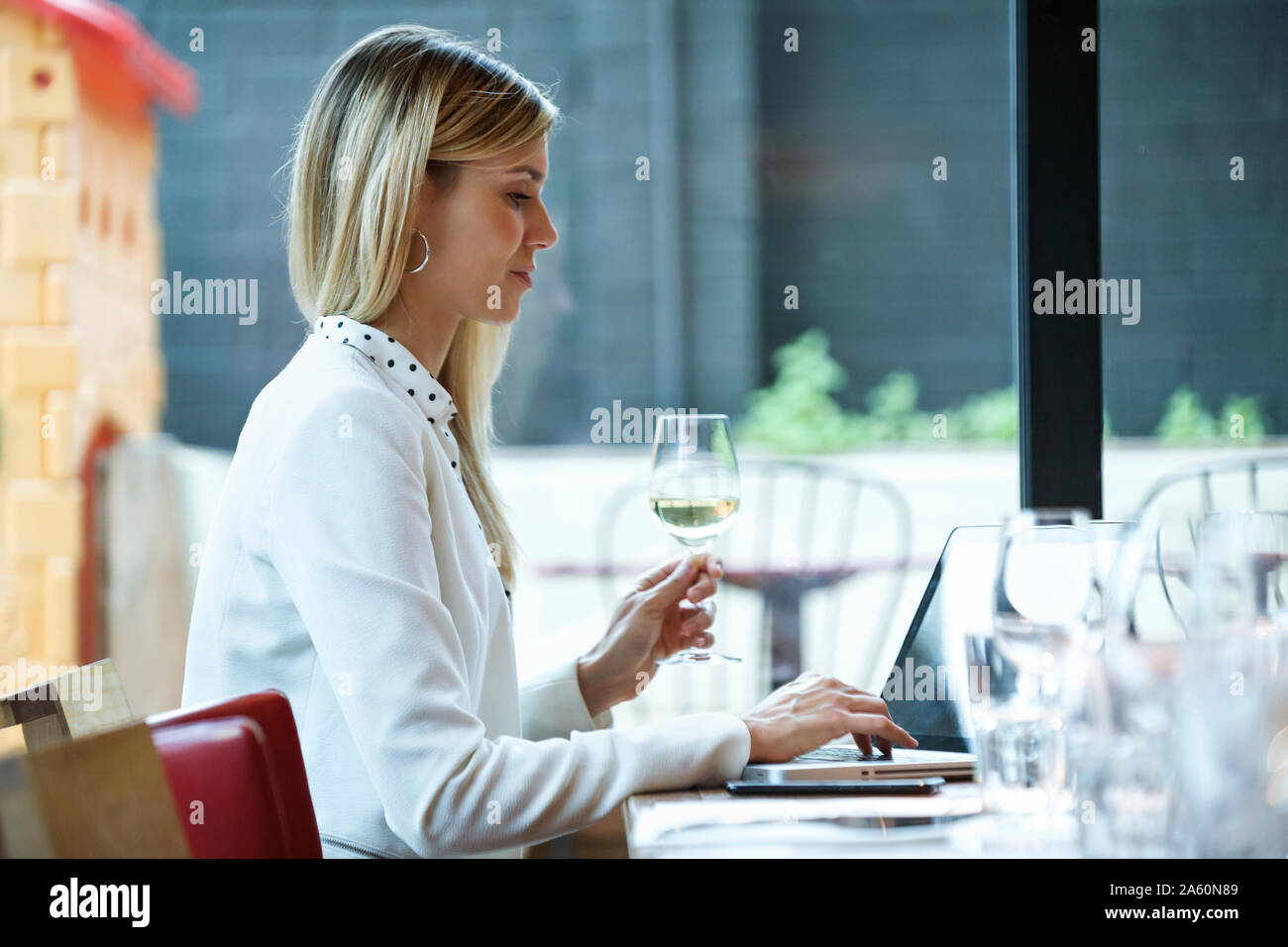 Businesswoman using laptop dans un restaurant tout en buvant du vin blanc Banque D'Images