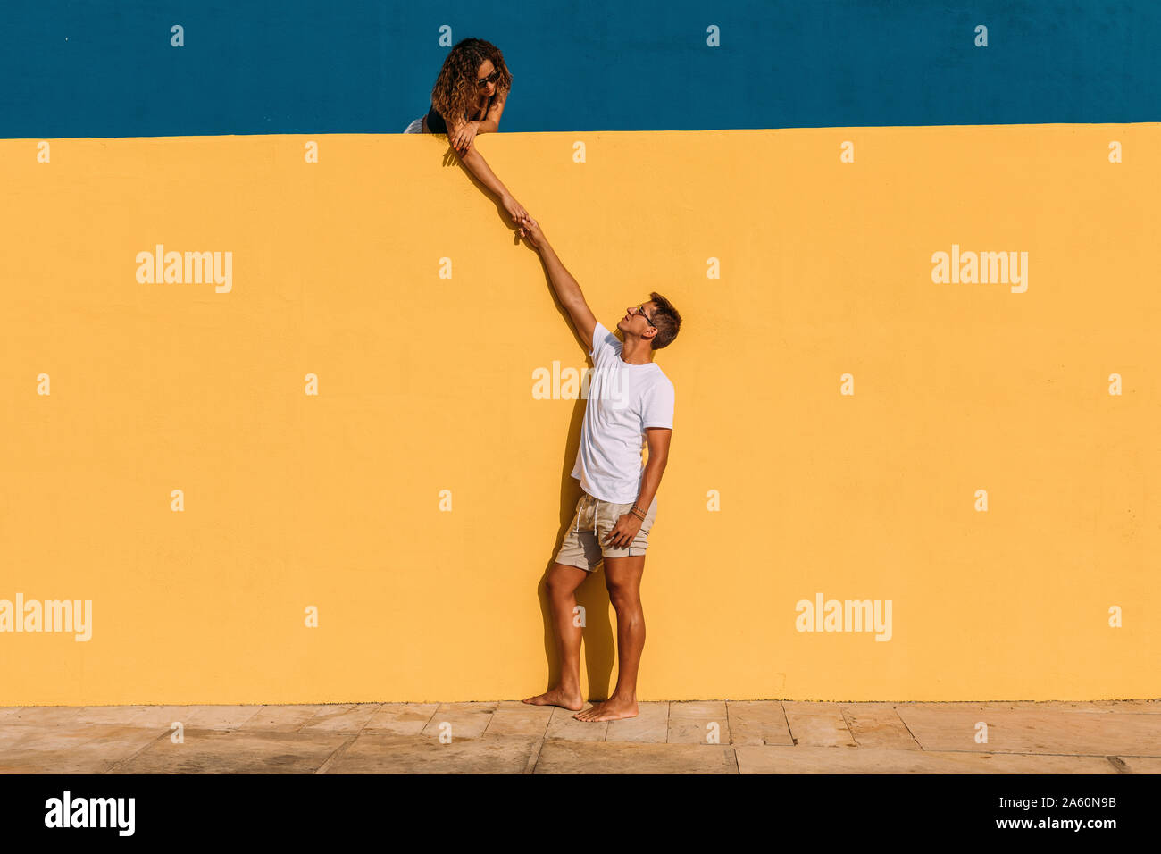 Jeune homme et femme derrière un mur jaune holding hands Banque D'Images