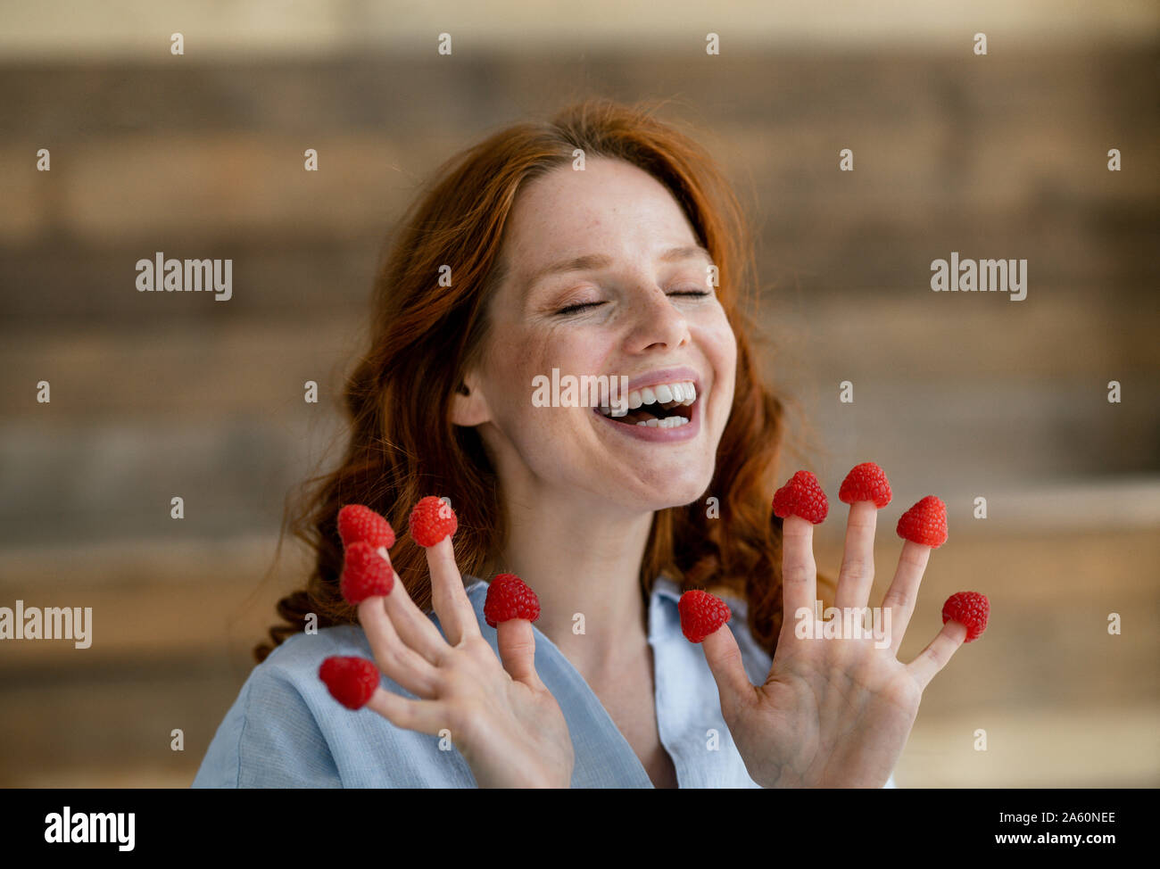 Portrait de femme rousse riant avec framboises sur ses doigts Banque D'Images