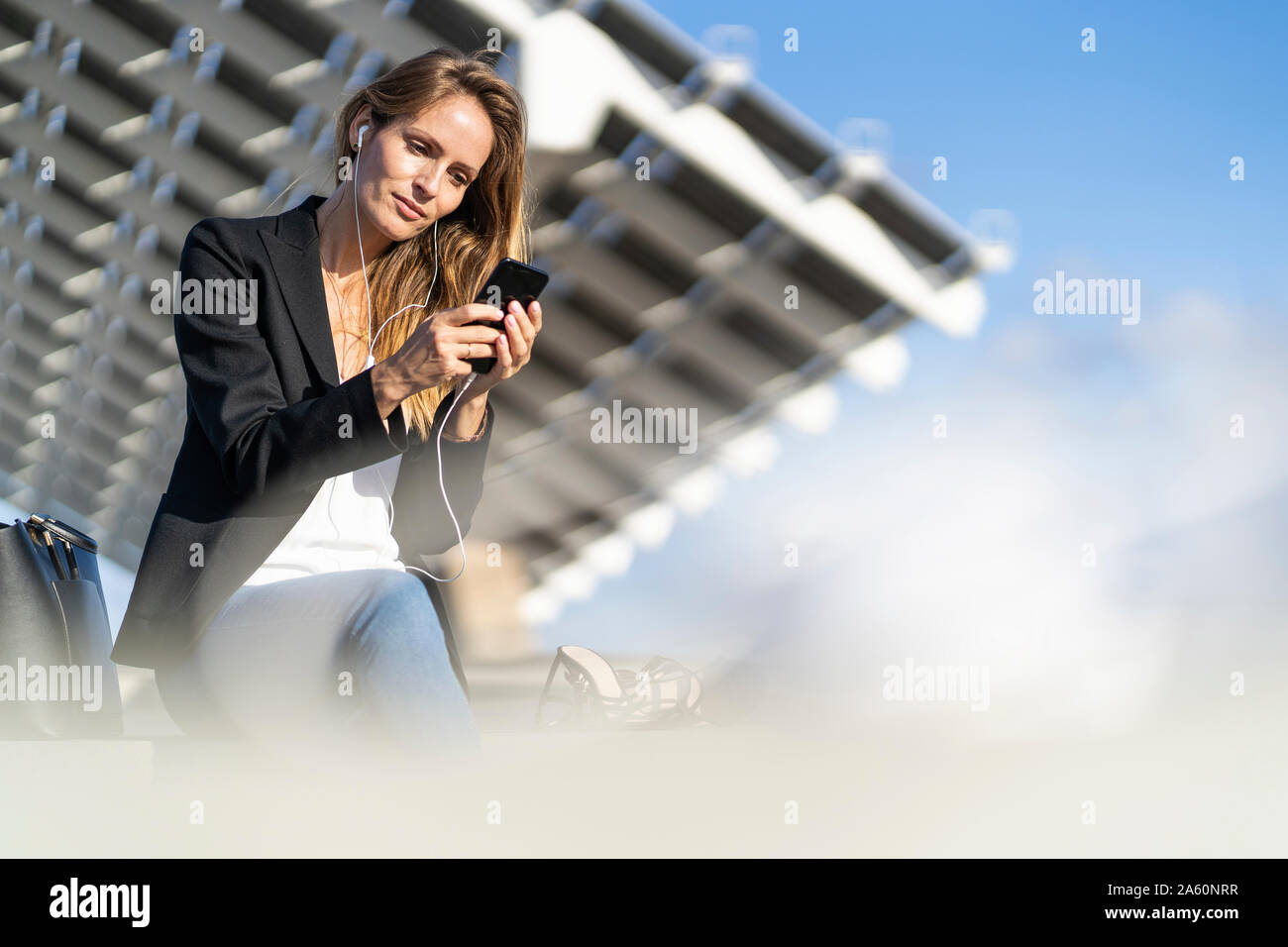 Businesswoman assis sur un mur avec le smartphone et écouteurs Banque D'Images
