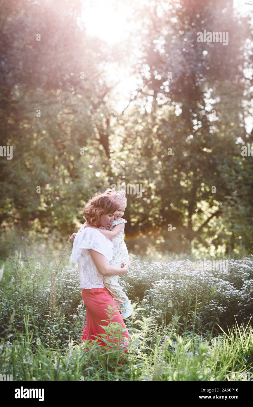 Mère portant sa fille dans une prairie de fleurs Banque D'Images