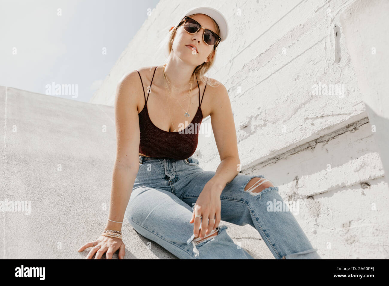 Jeune femme assise en face d'un mur blanc à l'extérieur Banque D'Images