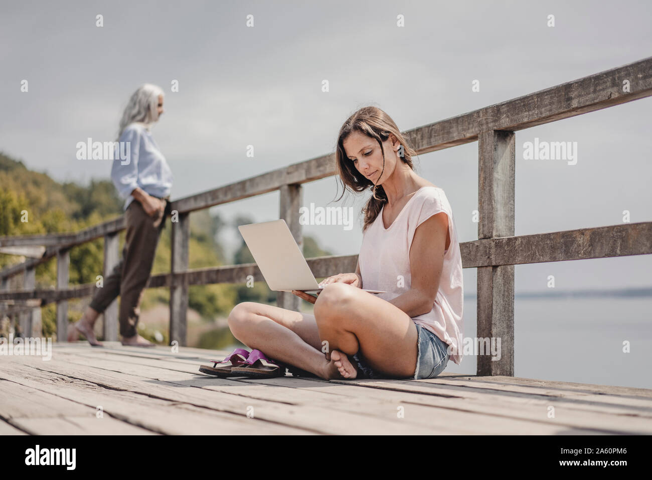 Femme assise sur le pont en bois, à l'aide d'un ordinateur portable, de mère Banque D'Images