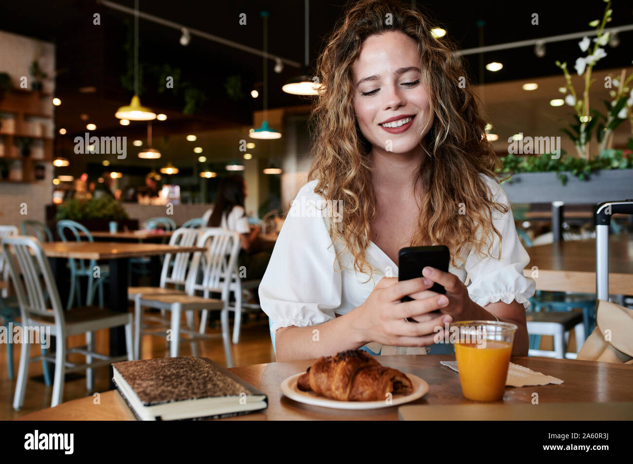 Smiling young woman using smartphone dans un café pendant le petit-déjeuner Banque D'Images