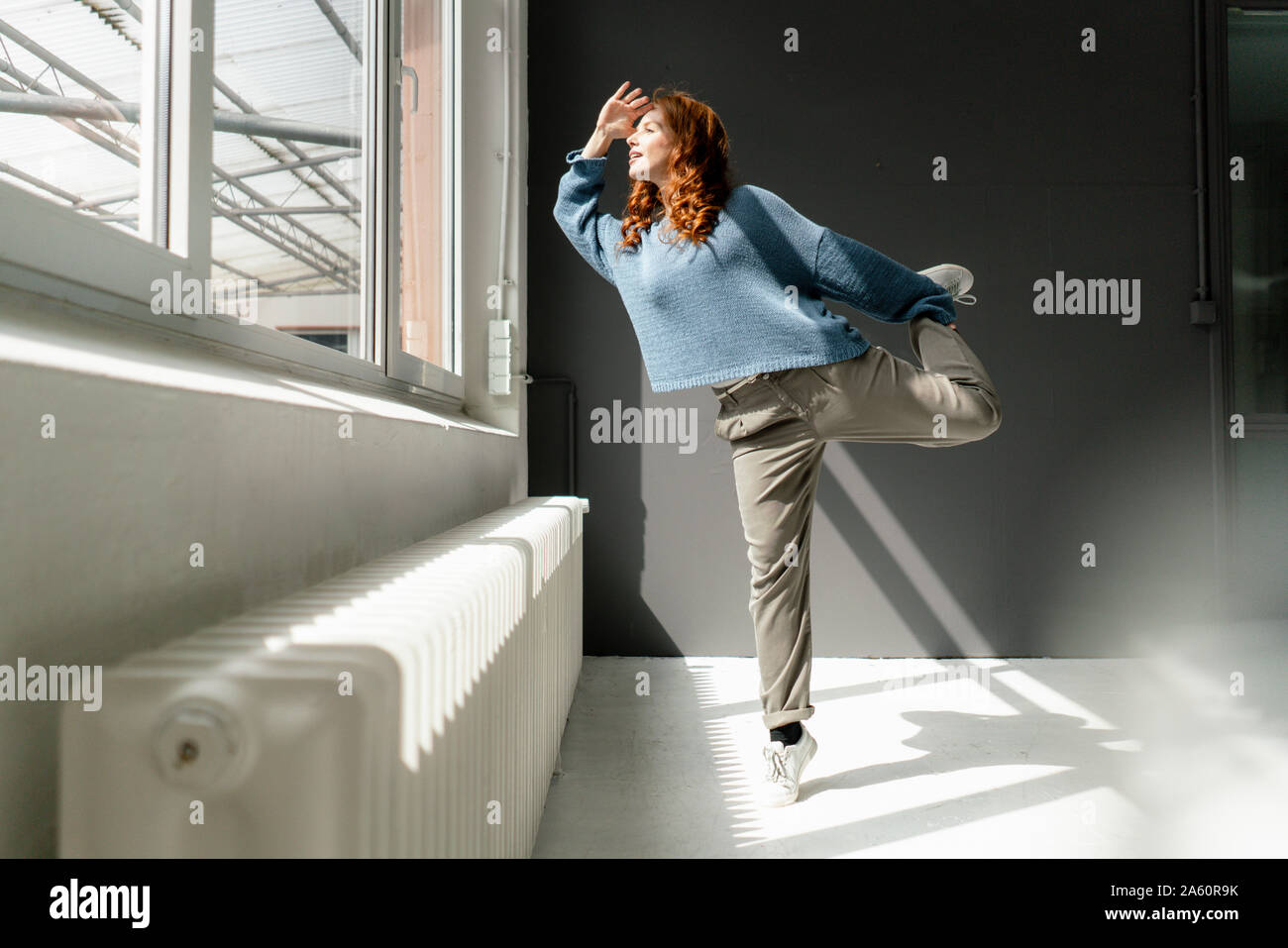 Femme rousse debout sur une jambe dans un loft à la fenêtre de Banque D'Images