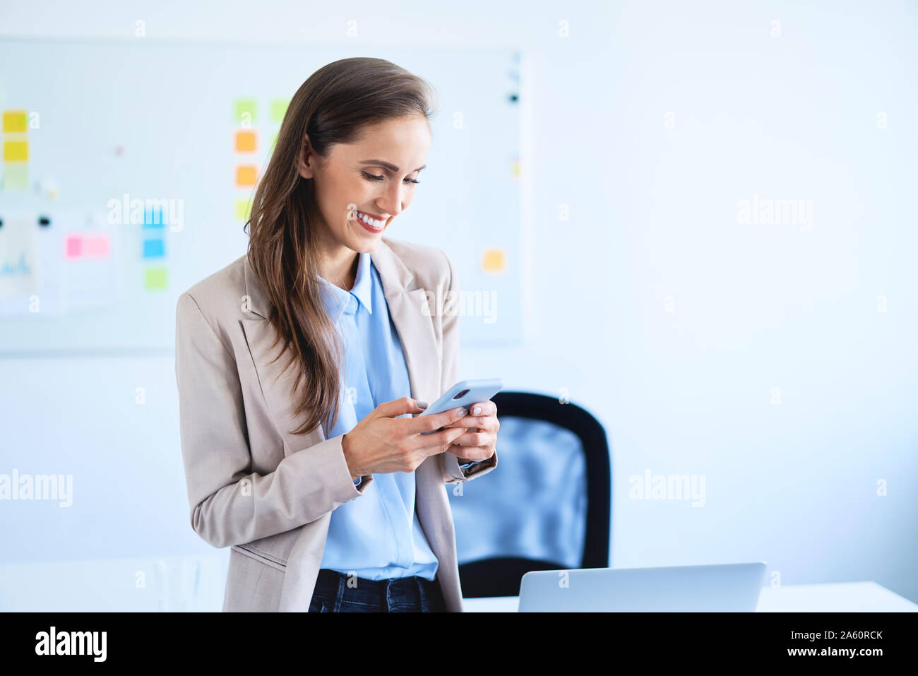 Smiling businesswoman standing in office using smartphone Banque D'Images