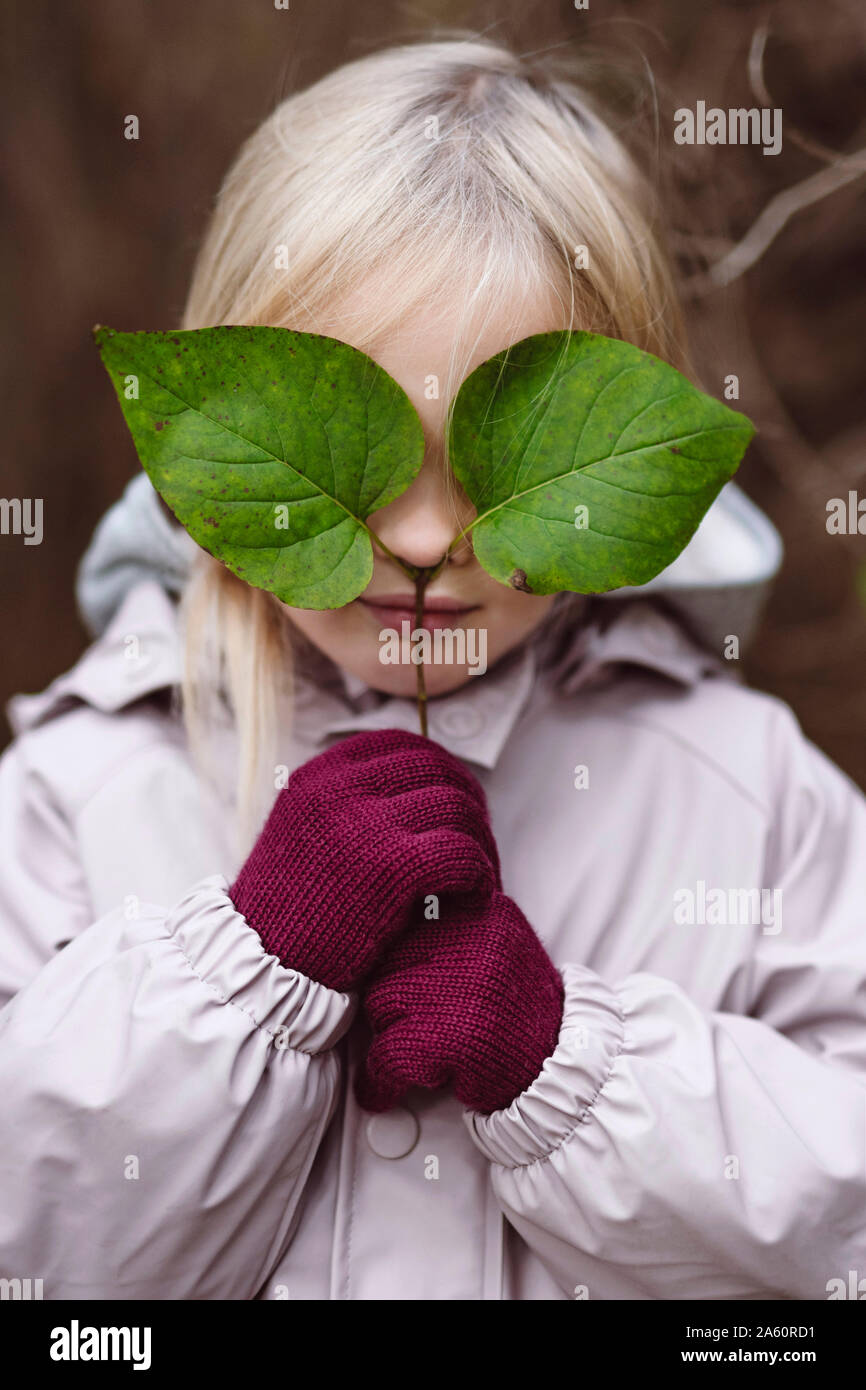 Portrait de petite fille blonde couvrant ses yeux avec des feuilles vertes Banque D'Images