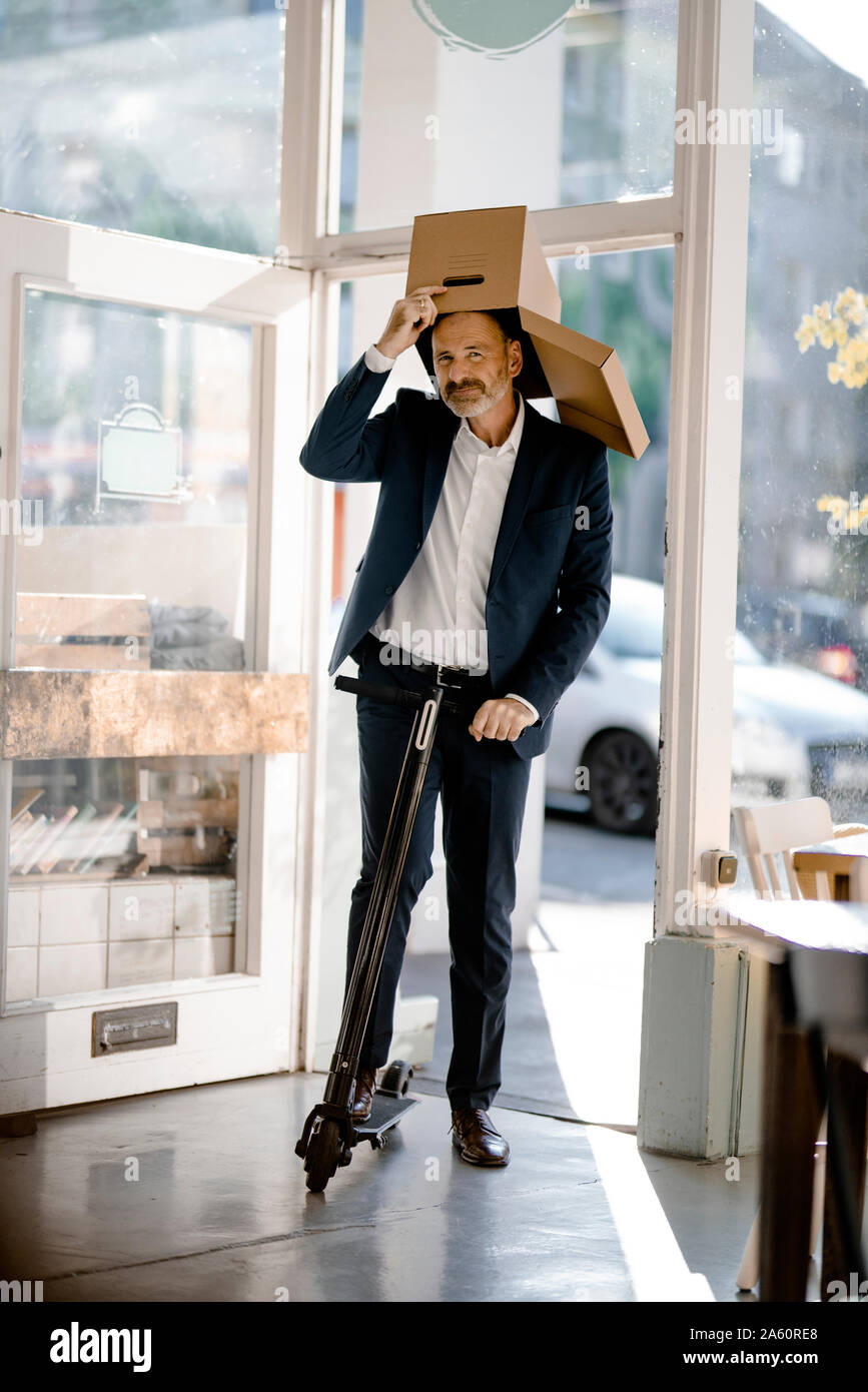 Businessman avec boîte en carton sur la tête, école e-scooter dans un café Banque D'Images