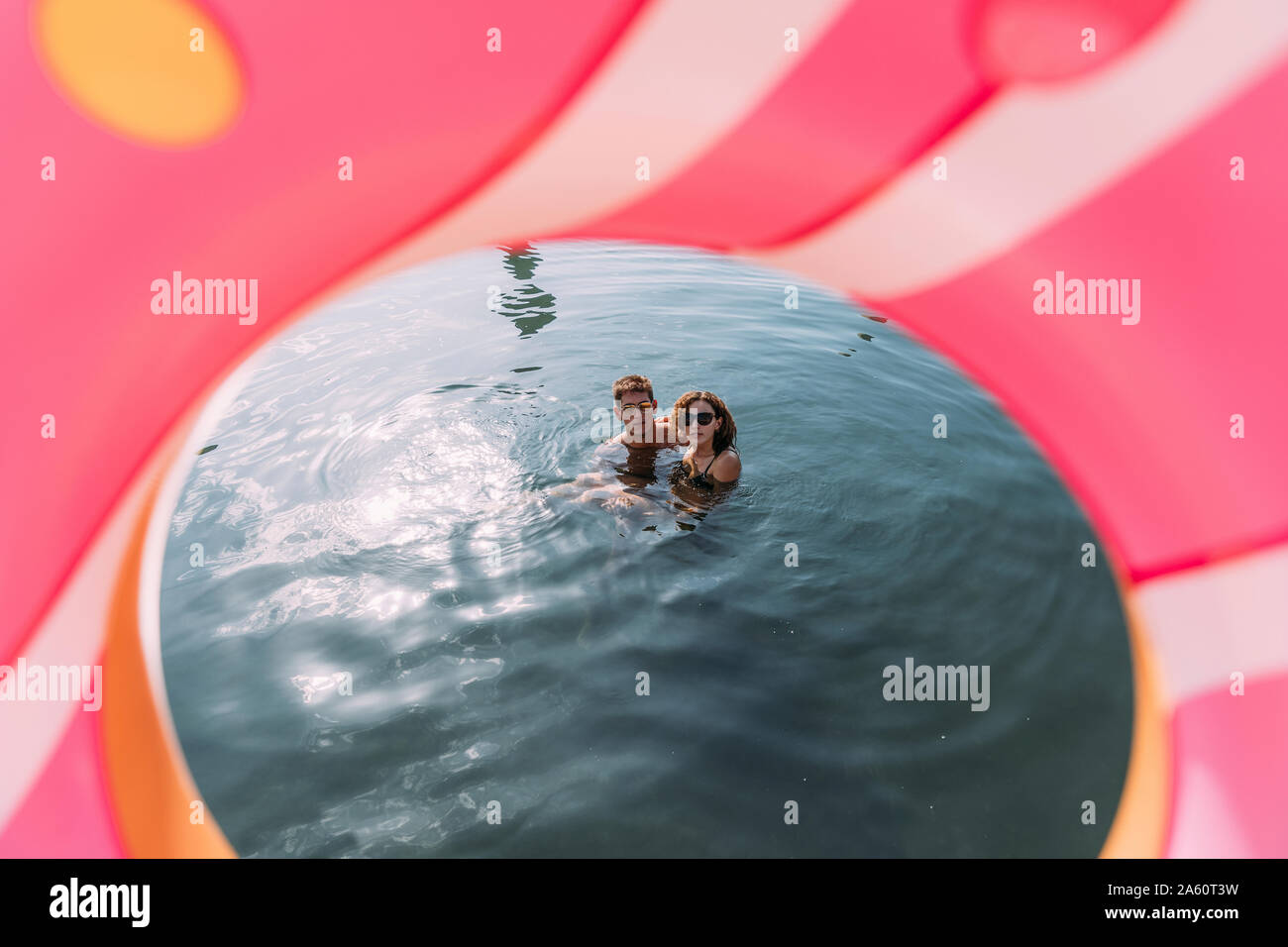 Jeune couple baignade en mer derrière flotter dans la forme donut gonflable Banque D'Images