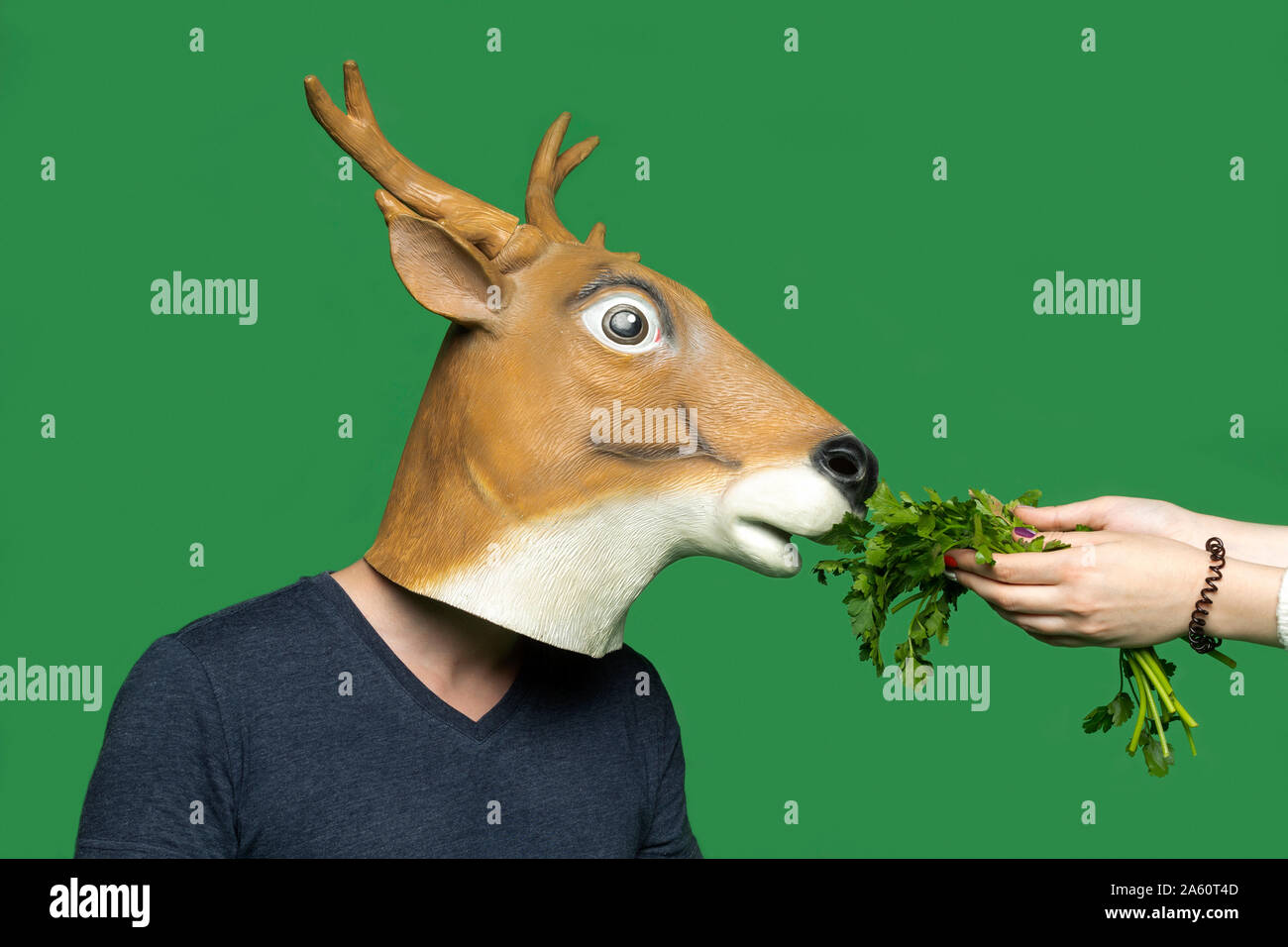 Jeune homme portant un masque de cerf qui sent le persil en face de fond vert Banque D'Images