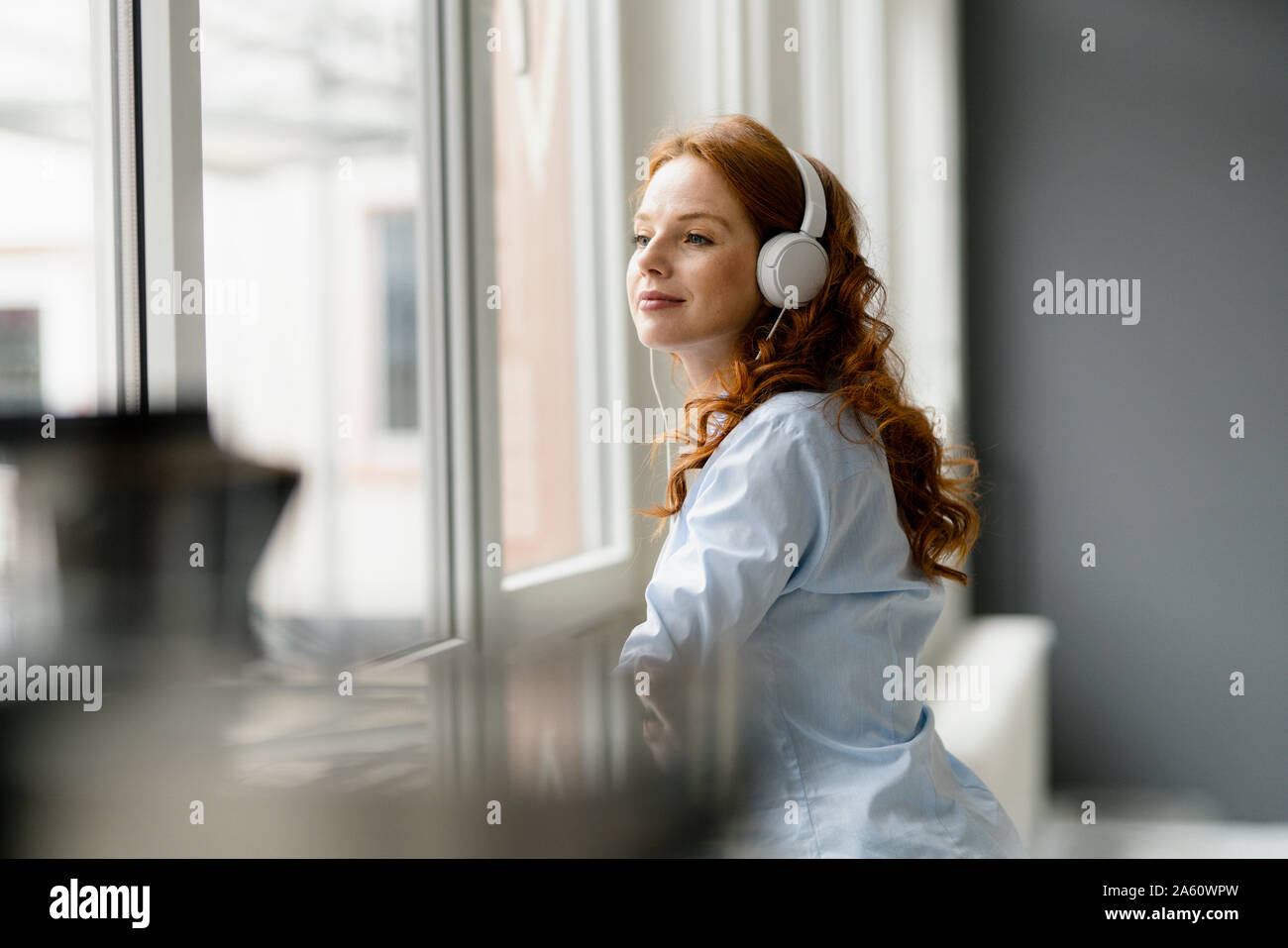 Portrait de femme rousse de l'écoute au casque de la musique tout en regardant par la fenêtre de Banque D'Images