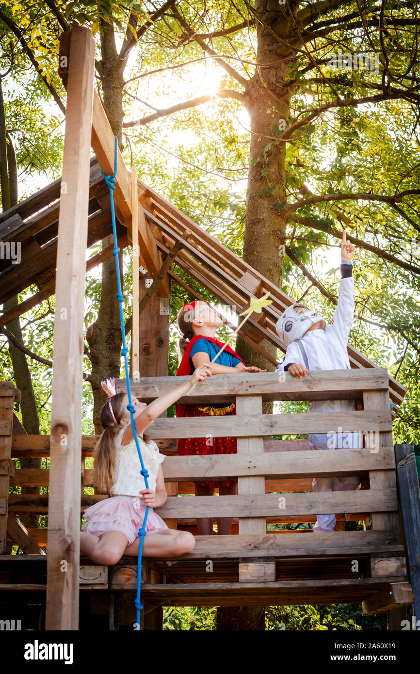 Trois enfants avec des costumes de super-héros jouant sur leur maison de l'arbre Banque D'Images